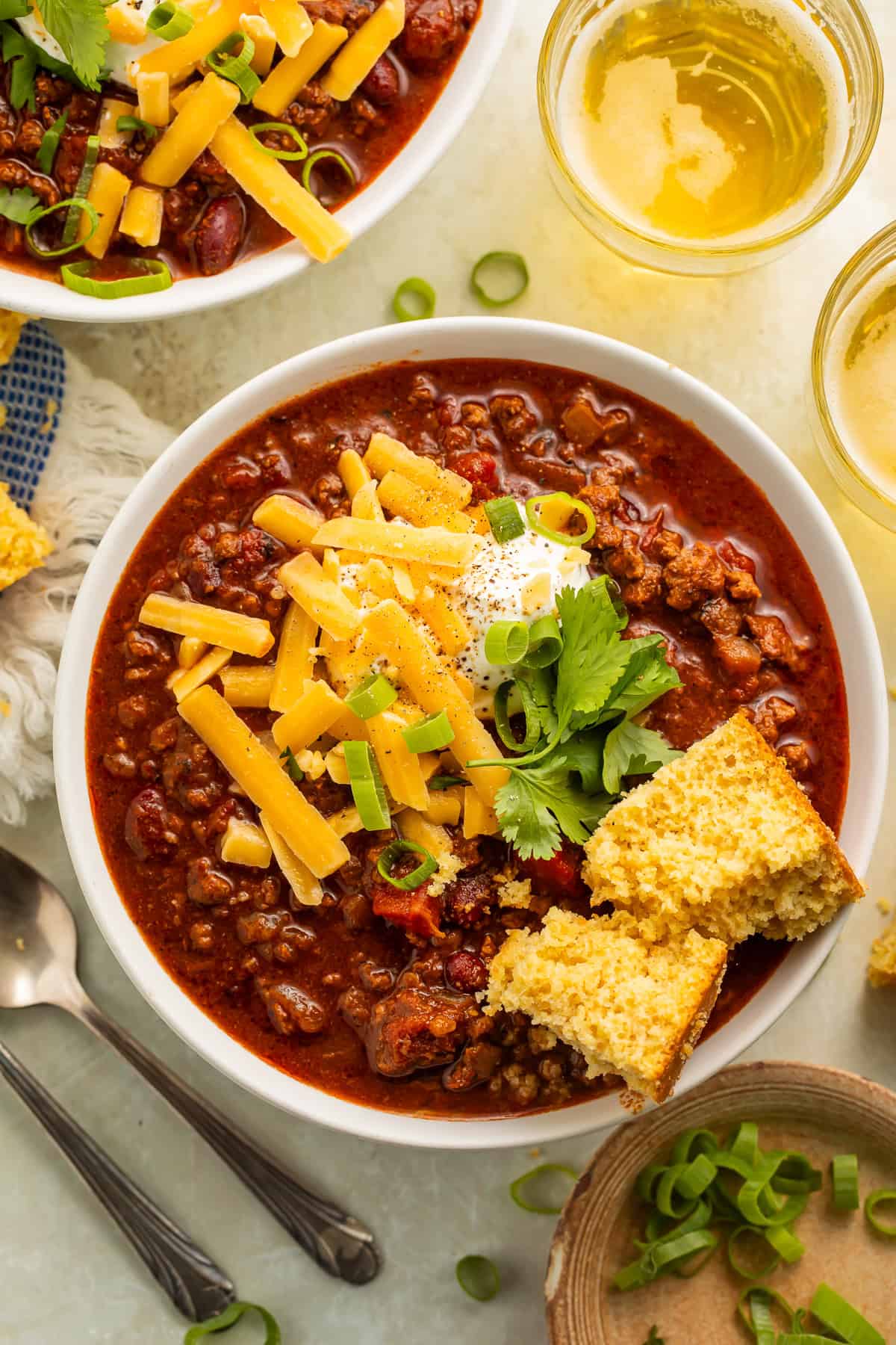 Bowl of gluten free chili with cornbread, green onions, sour cream and shredded cheese.