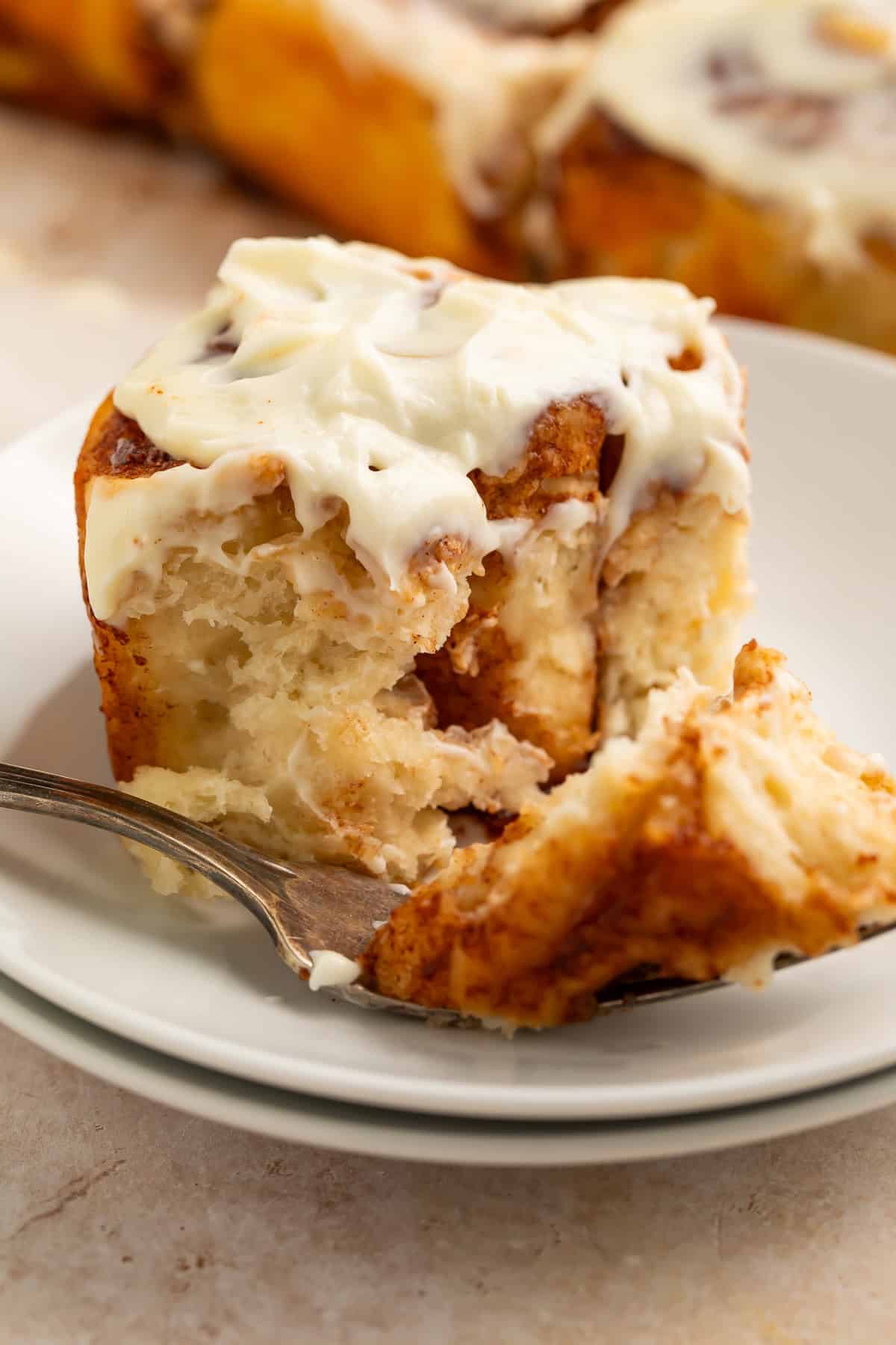 Healthy cinnamon roll on a white plate with a forkful taken out the side.