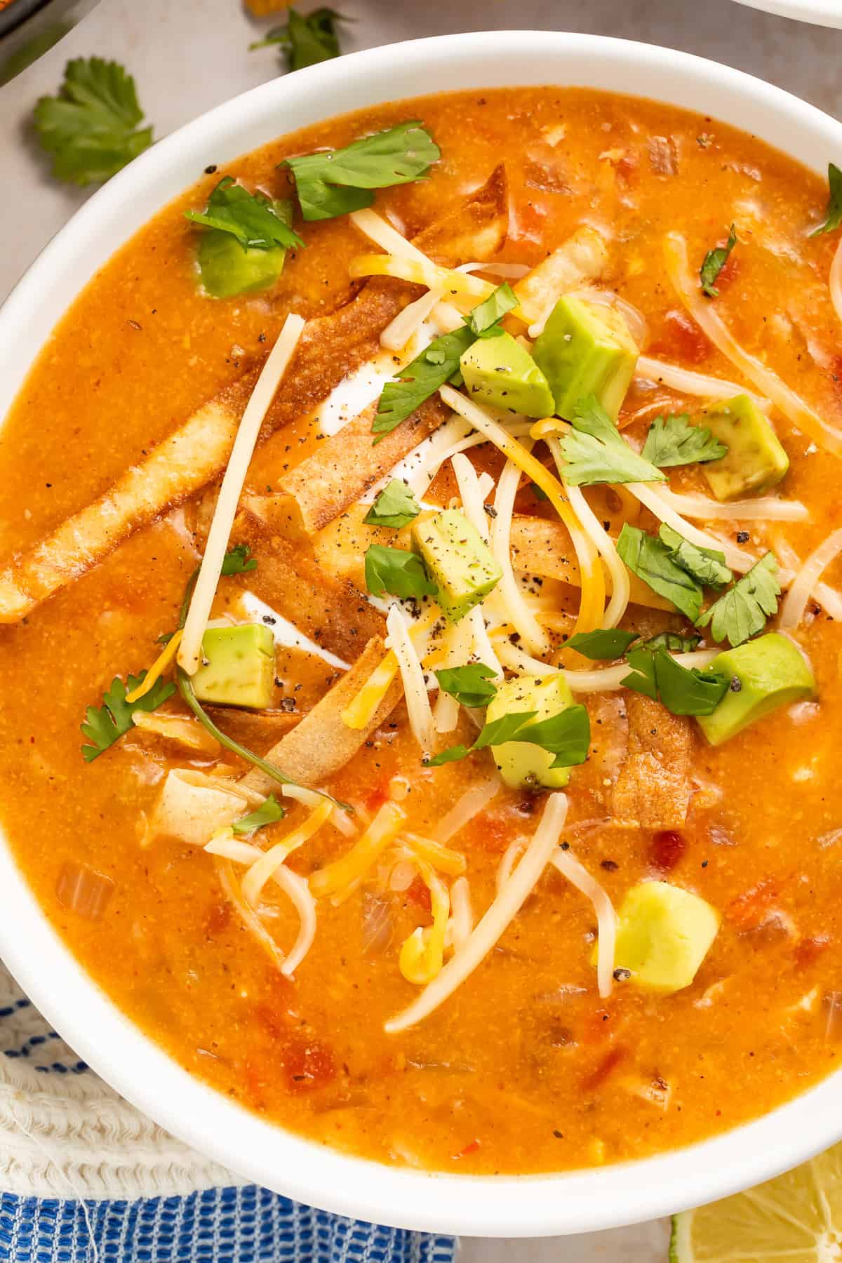 Close up of a bowl of creamy chicken tortilla soup topped with shredded cheese, diced avocado and cilantro.