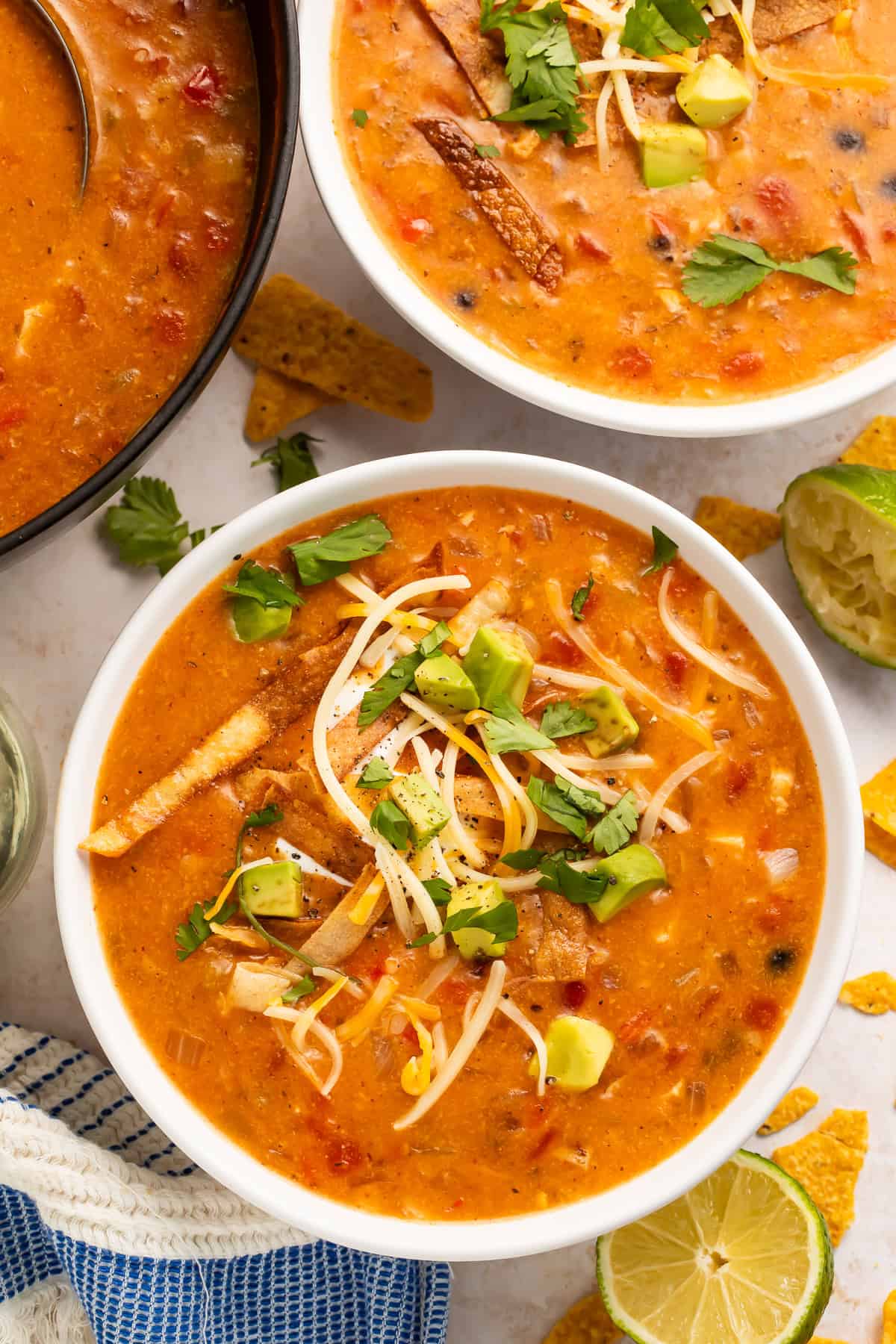 Two bowls of chicken tortilla soup with all the fixings, with the pot of soup visible off to one side.