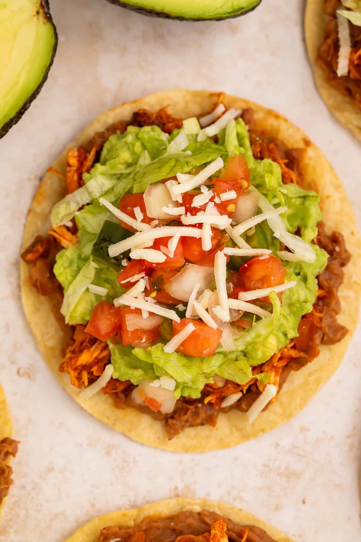 Close up of a chicken tostada topped with guacamole, salsa and shredded cheese.
