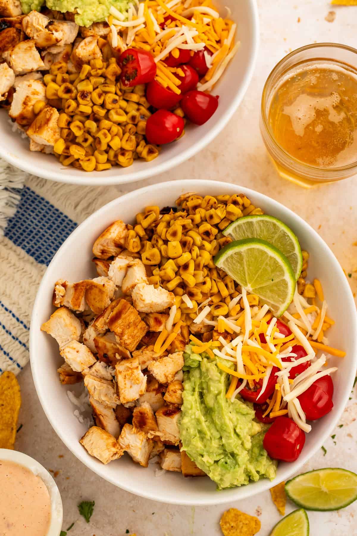 Rice bowls topped with chopped chicken, guacamole, cooked tomatoes, charred corn, shredded cheese and lime wedges.