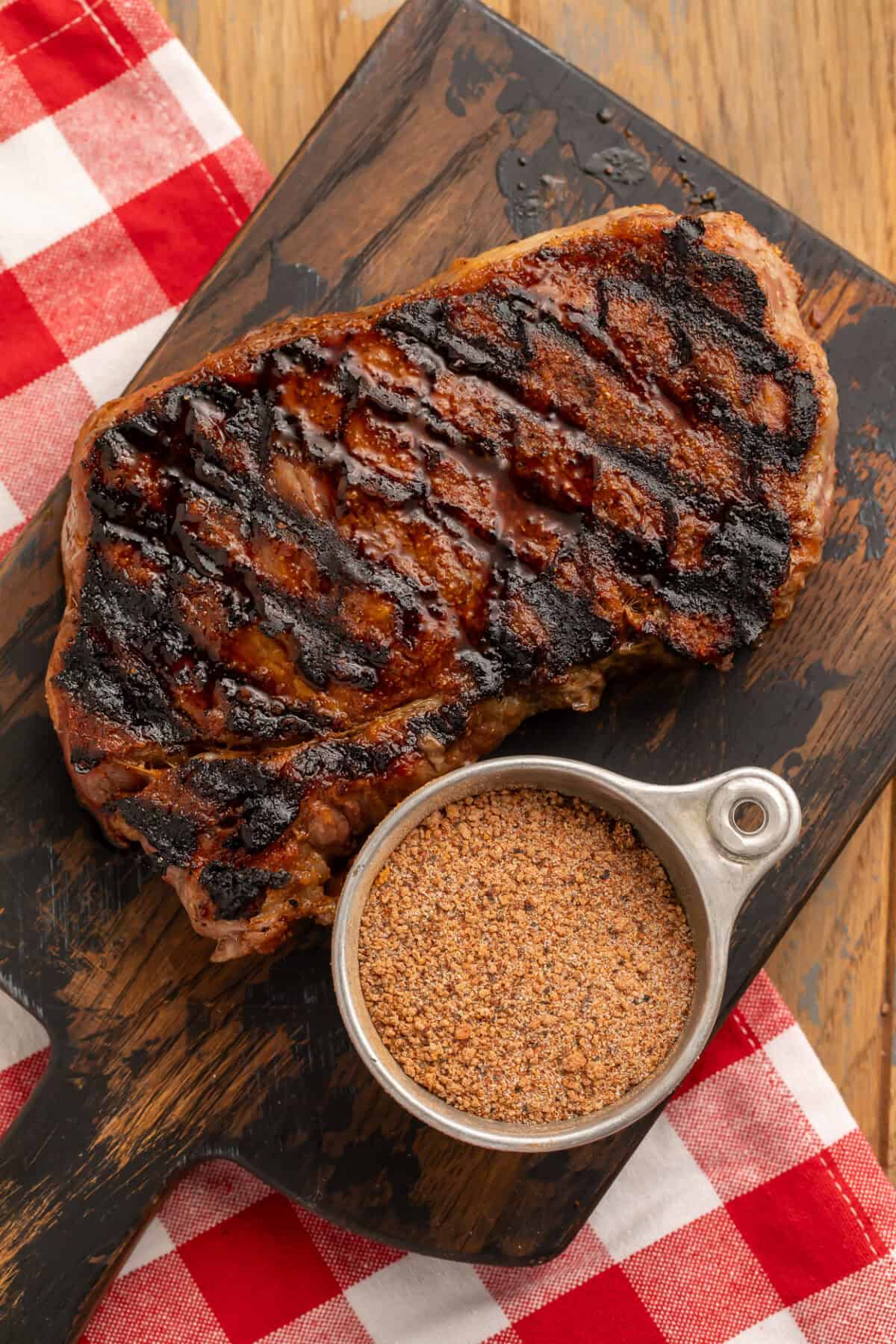 Grilled steak on a wooden board with a cup of steak seasoning.