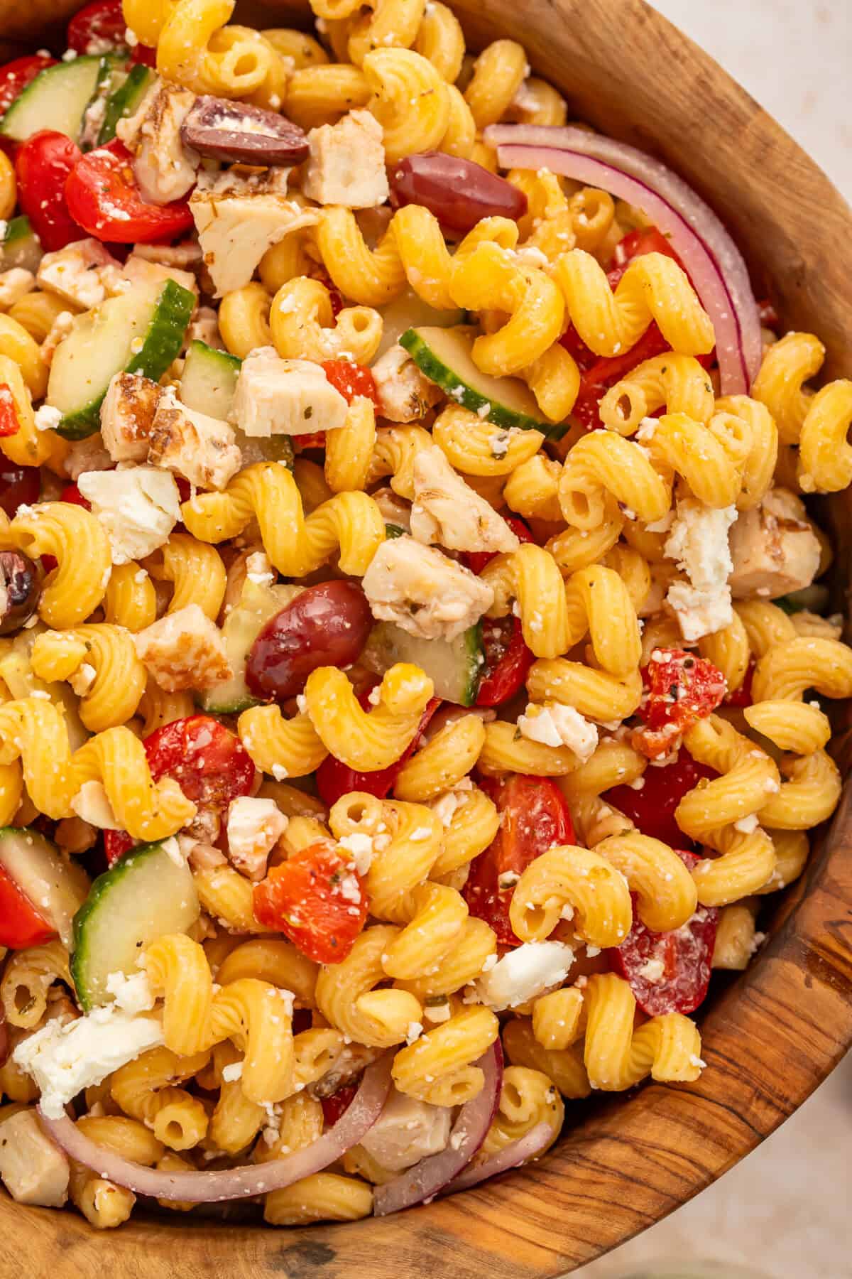 Close up of pasta salad with chicken, onions, olives and feta