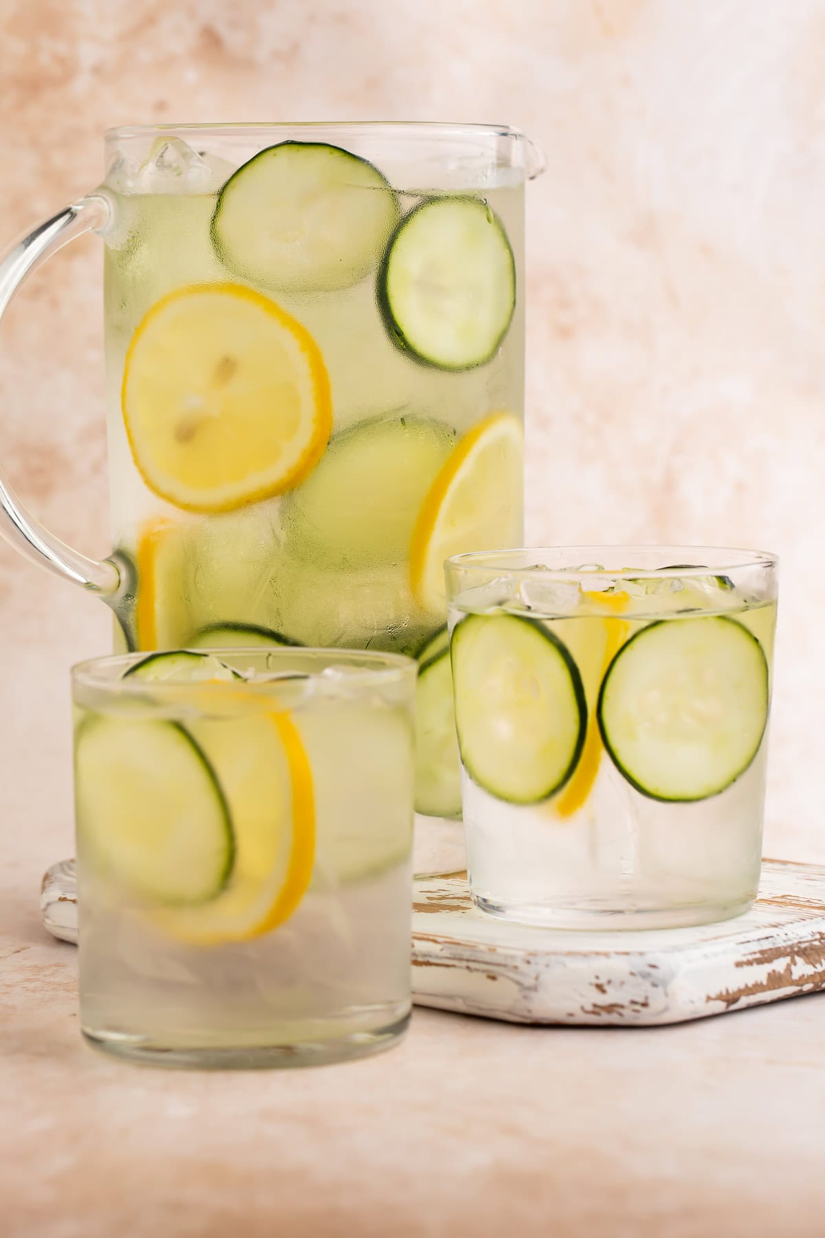 Jug of lemon and cucumber infused water with two glasses of the cucumber water in the foreground.