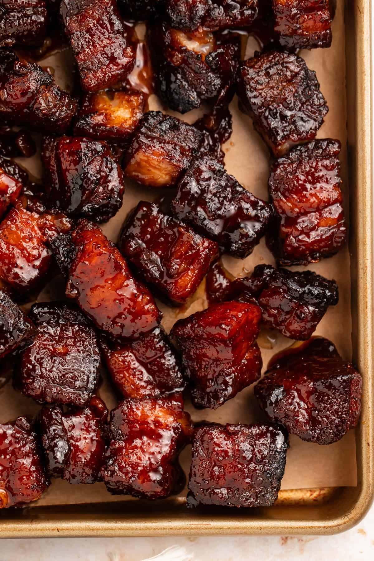 Close up of pork belly burnt ends on a lined baking sheet.