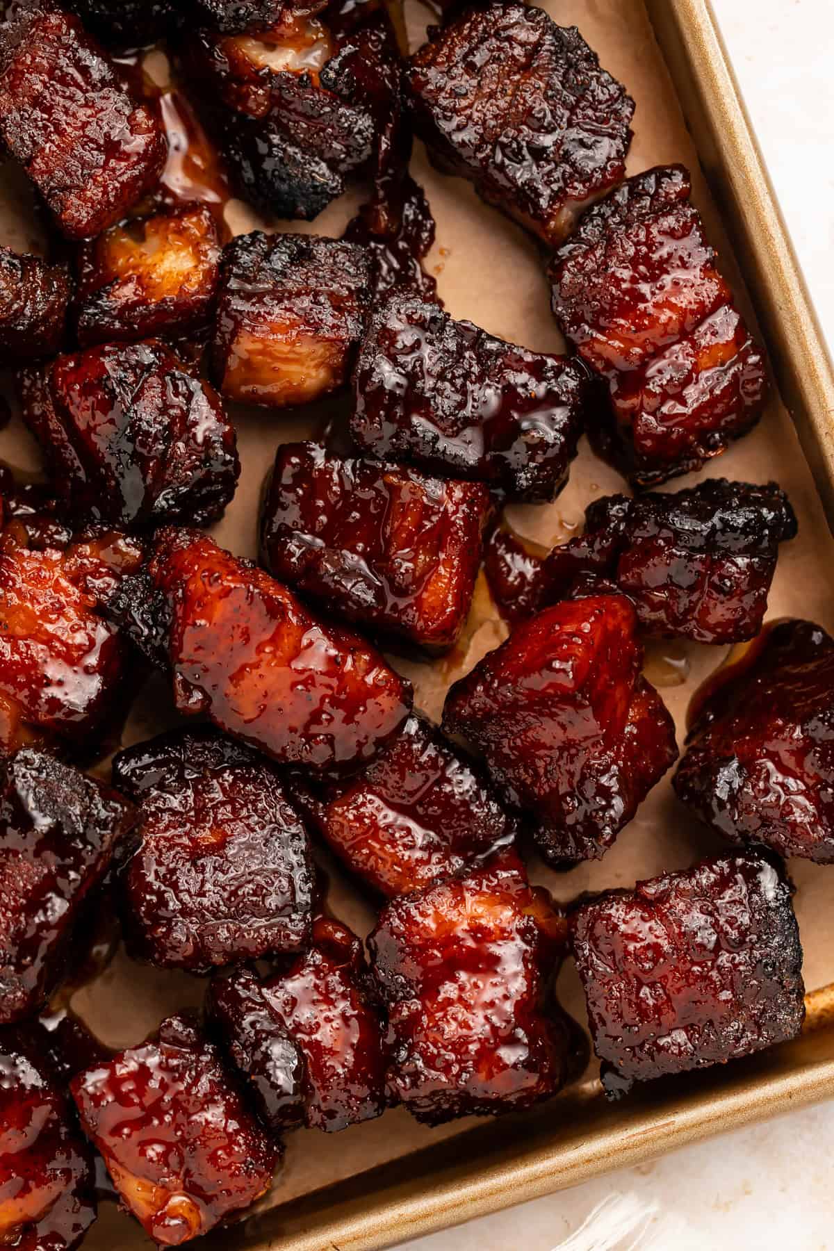 Close up of glossy smoked pork belly burnt ends on a baking sheet.