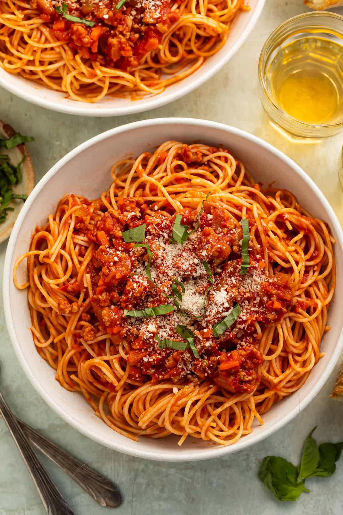 Close up of a bowl of spaghetti in tomato sauce with ground turkey. It is topped with parmesan and shredded basil.