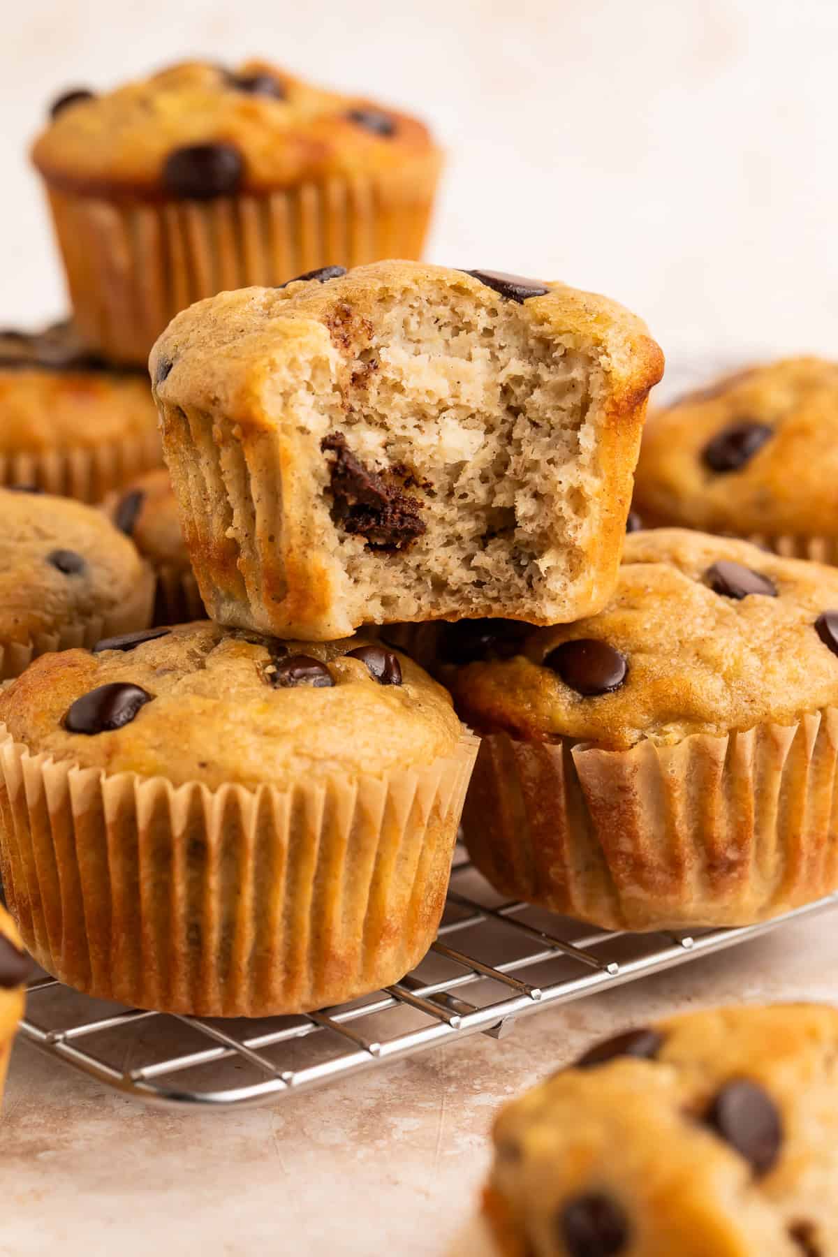 Stacked banana chocolate chip muffins. The top muffin has a bite taken out of it to show the middle.