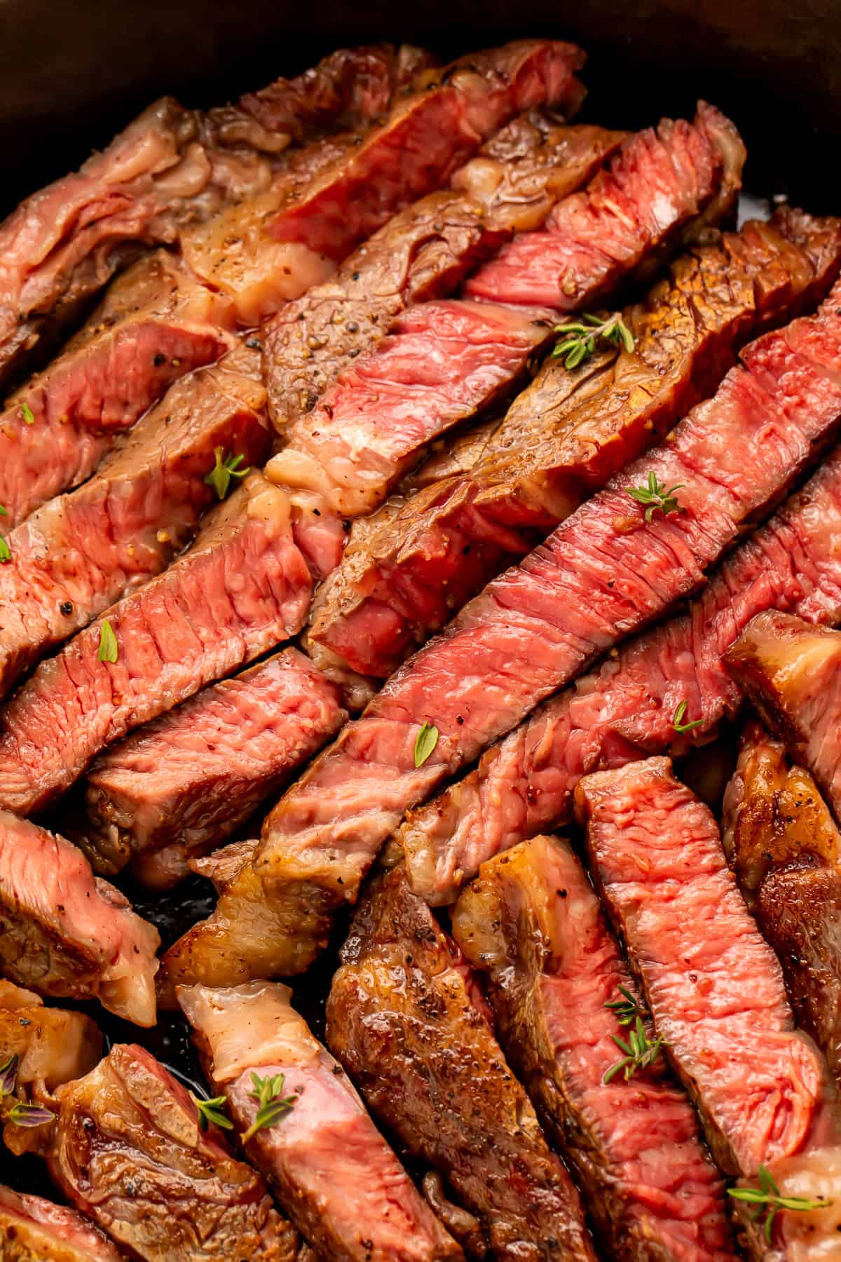 Close up of slices of rare rib eye steak sprinkled with fresh thyme leaves.