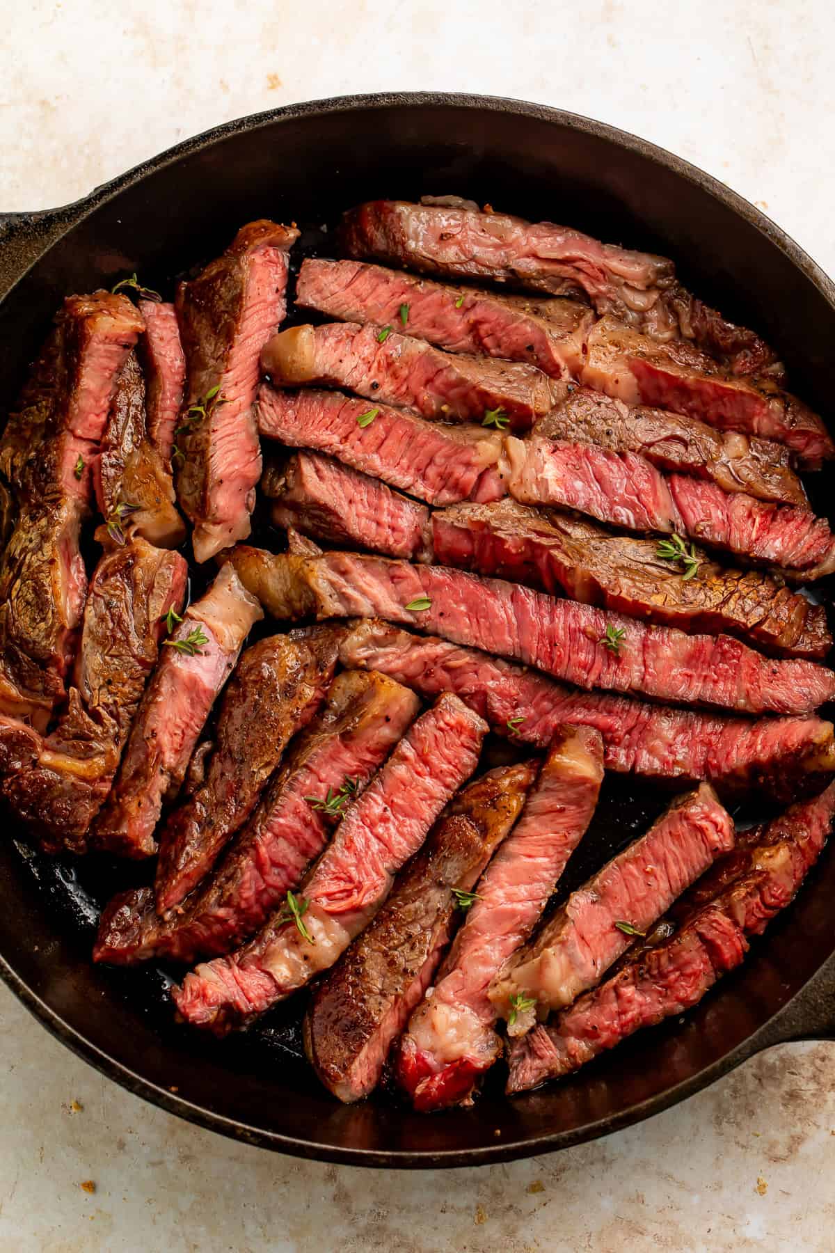 Cast iron skillet of medium rare rib eye steak slices.