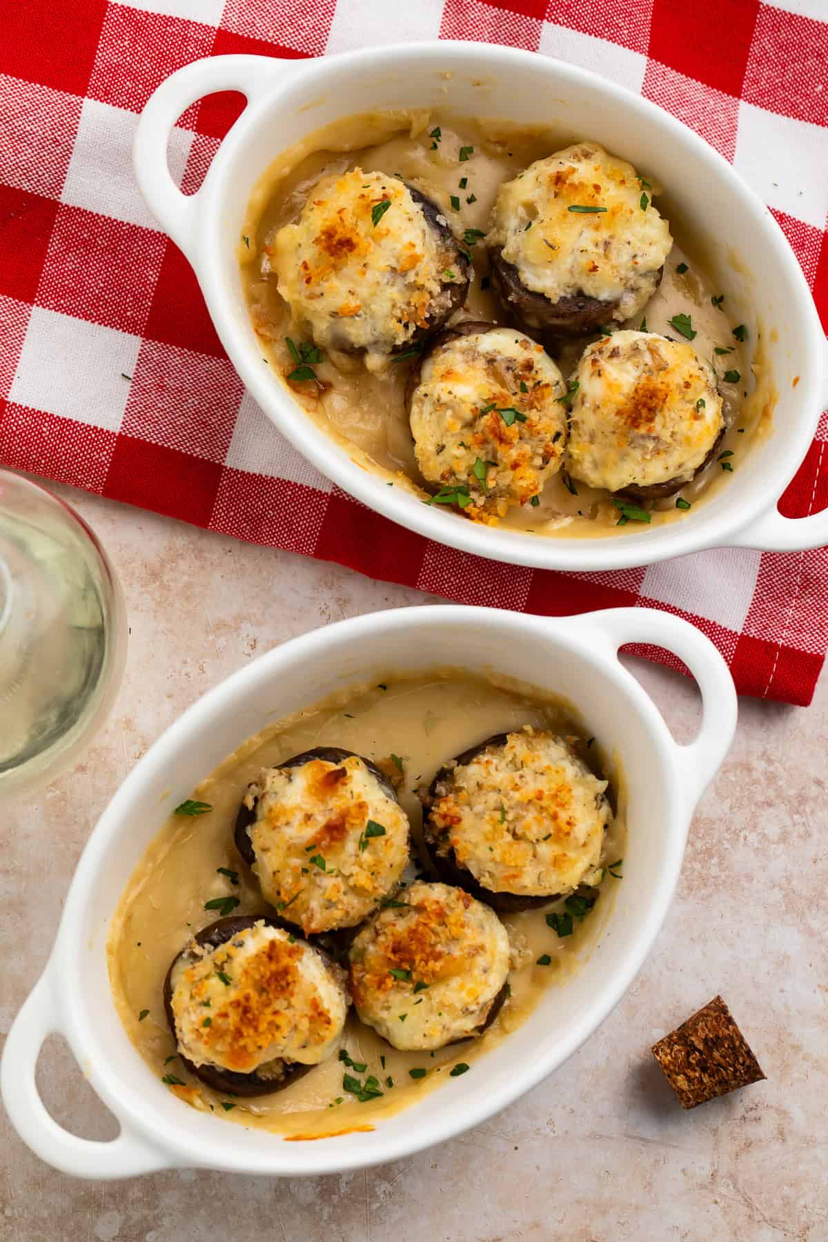 Two dishes of stuffed mushrooms with breadcrumb toppings on a white and red checked cloth.