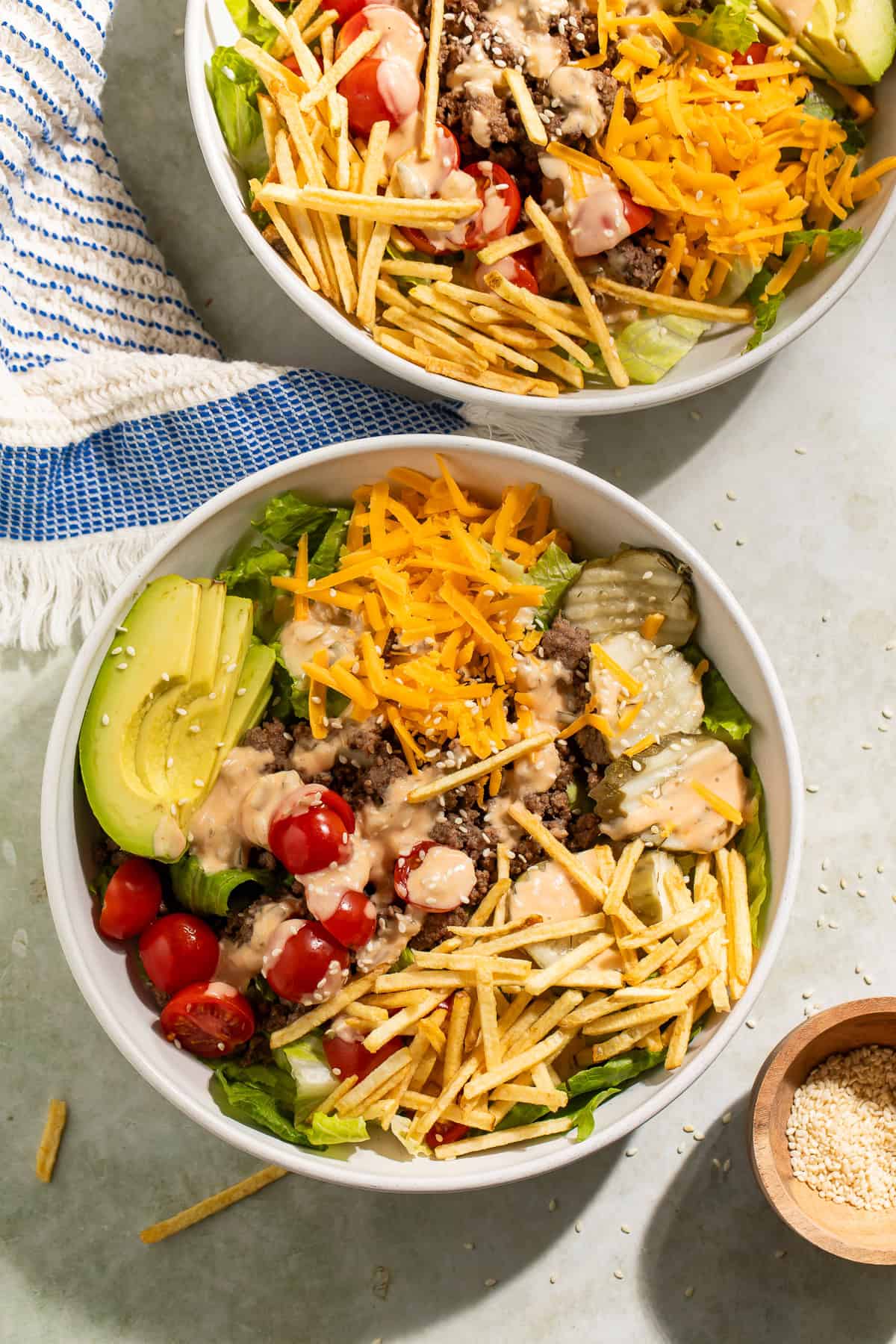 Burger bowls made with ground beef, lettuce, cheddar cheese, avocado, cherry tomatoes, pickles, crispy potato sticks, and burger sauce