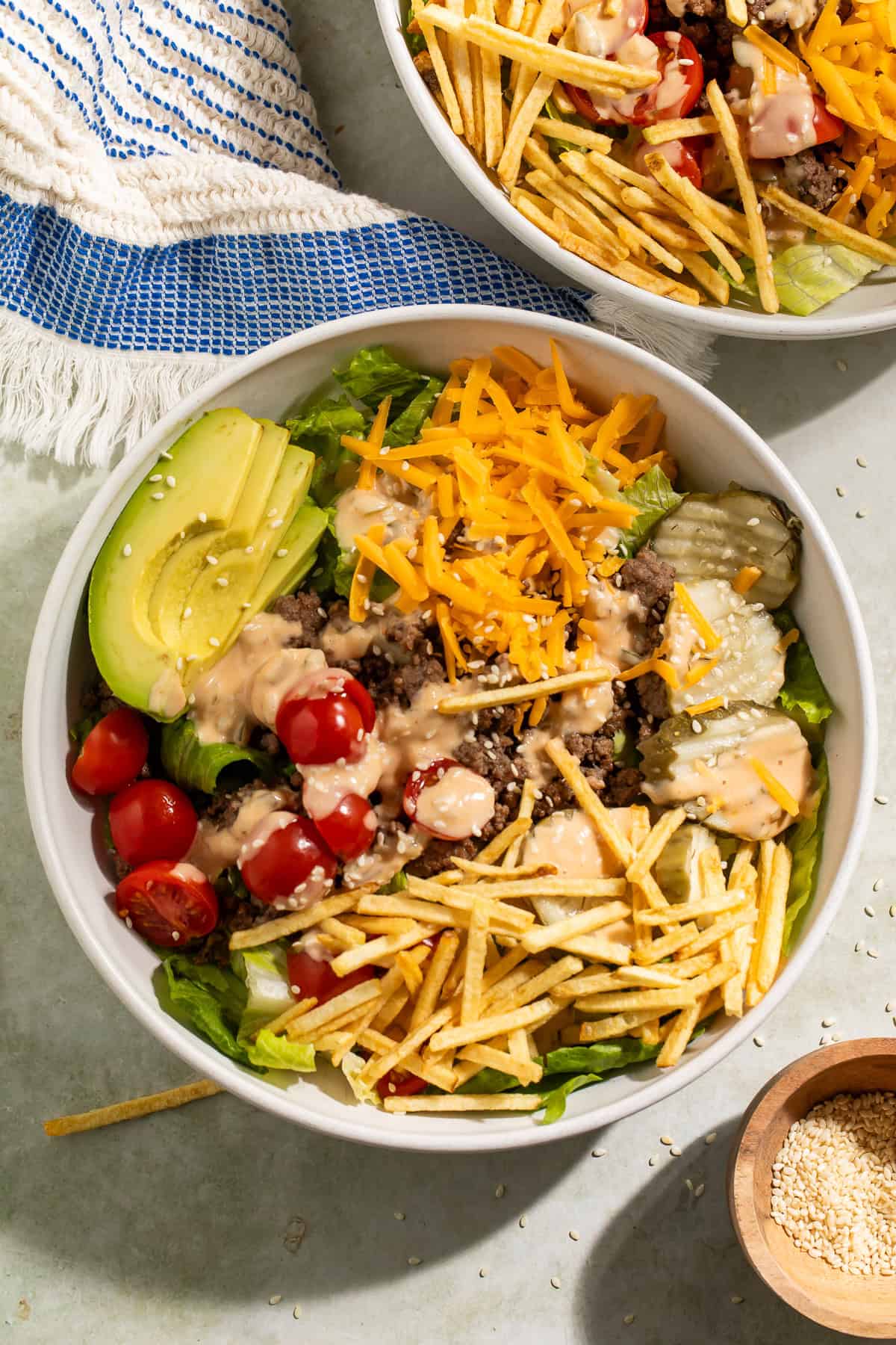Close-up of a burger bowl with ground beef, cheddar cheese, avocado, pickles, tomatoes, and crispy potato sticks