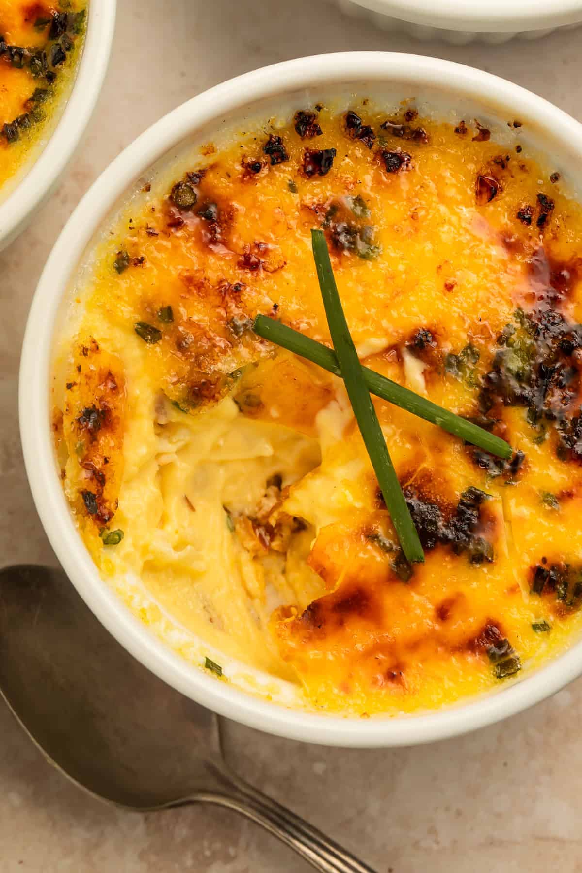 Close-up view of creamy crab brûlée with a browned cheesy topping in a white ramekin