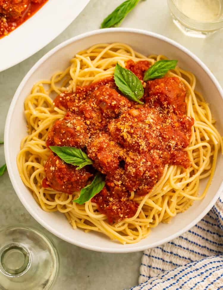 Gluten free meatballs in tomato sauce spooned over a bowl of spaghetti garnished with fresh basil leaves.