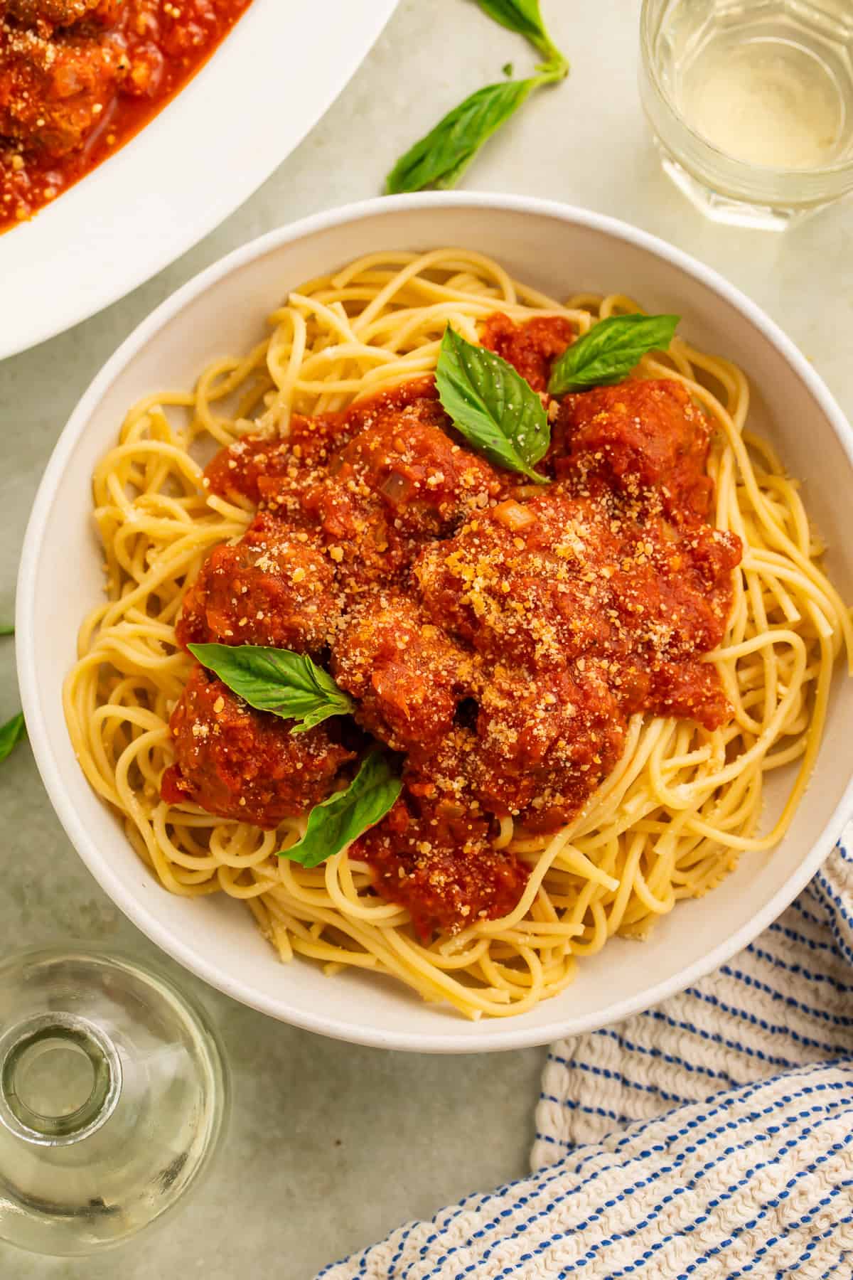 Gluten free meatballs in tomato sauce spooned over a bowl of spaghetti garnished with fresh basil leaves.