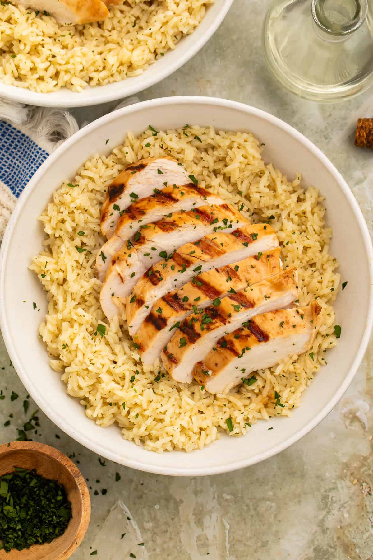 Grilled chicken breast sliced over seasoned rice in a white bowl with fresh parsley garnish.