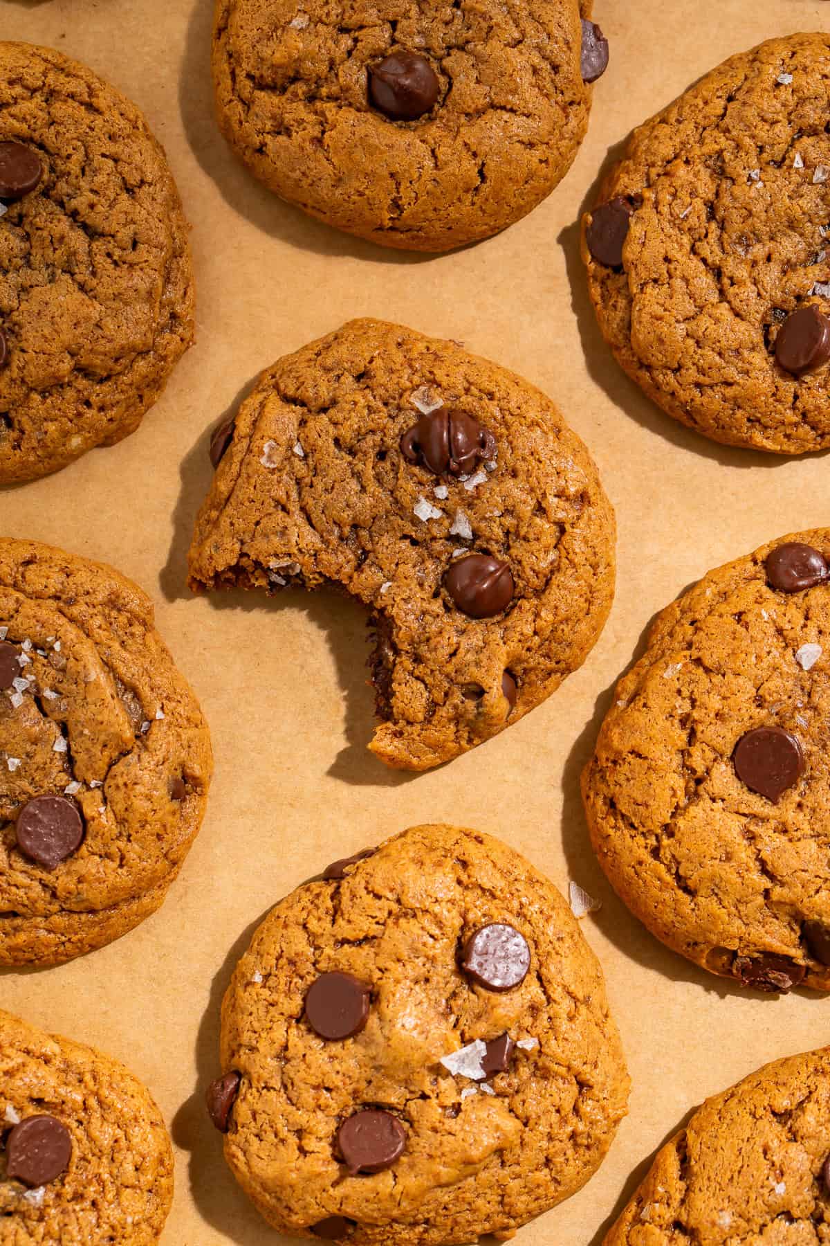Healthy chocolate chip cookies with dark chocolate chips and flaky sea salt arranged on parchment paper