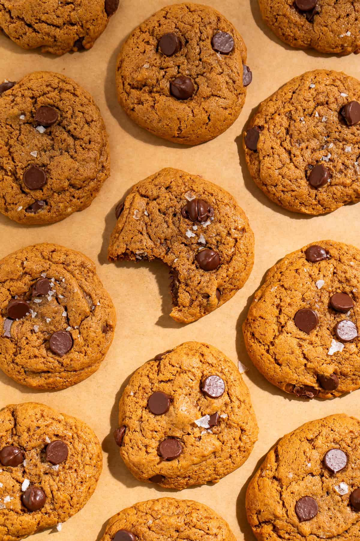 Batch of healthy chocolate chip cookies with chocolate chips and sea salt on parchment-lined baking surface.