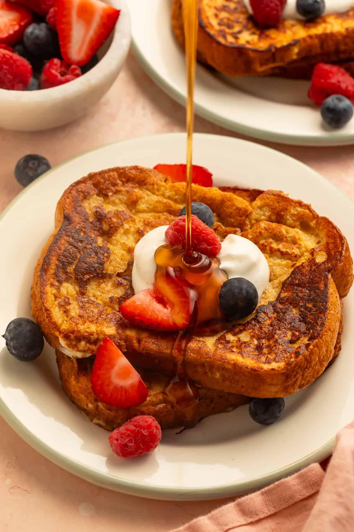 Healthy French toast topped with yogurt, strawberries, raspberries, and blueberries, drizzled with maple syrup