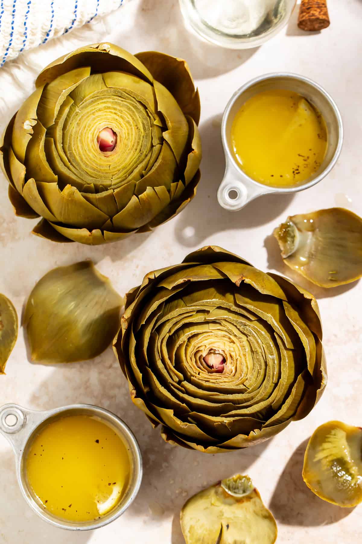 Cooked whole artichokes served with melted butter and artichoke leaves on a light countertop