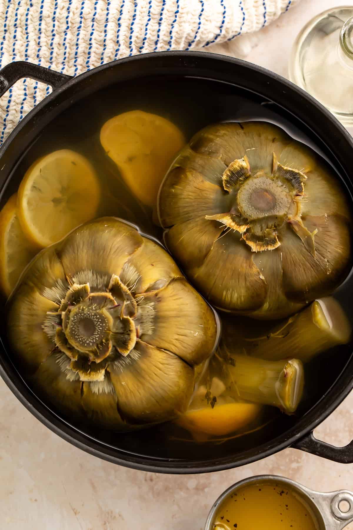 Whole artichokes boiling in a pot with lemon slices and garlic cloves