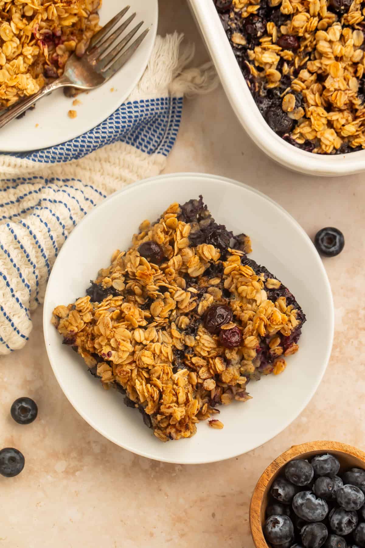 Blueberry baked oatmeal served in a bowl with fresh blueberries and a baking dish in the background