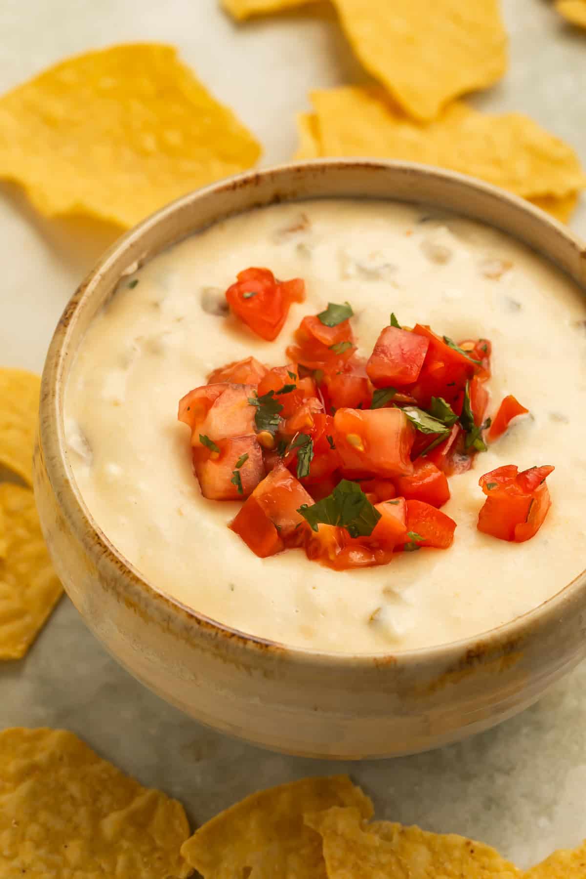 Creamy crockpot queso dip topped with diced tomatoes and cilantro, served in a bowl with tortilla chips