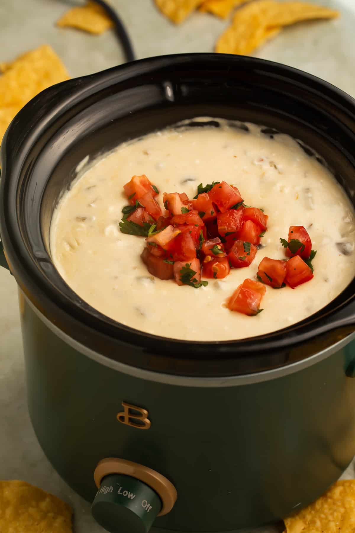 Crockpot queso dip topped with diced tomatoes and cilantro served directly in a slow cooker