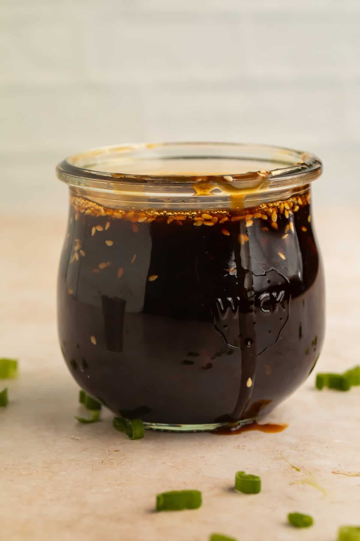 Homemade teriyaki sauce in a glass jar with sesame seeds and green onions.