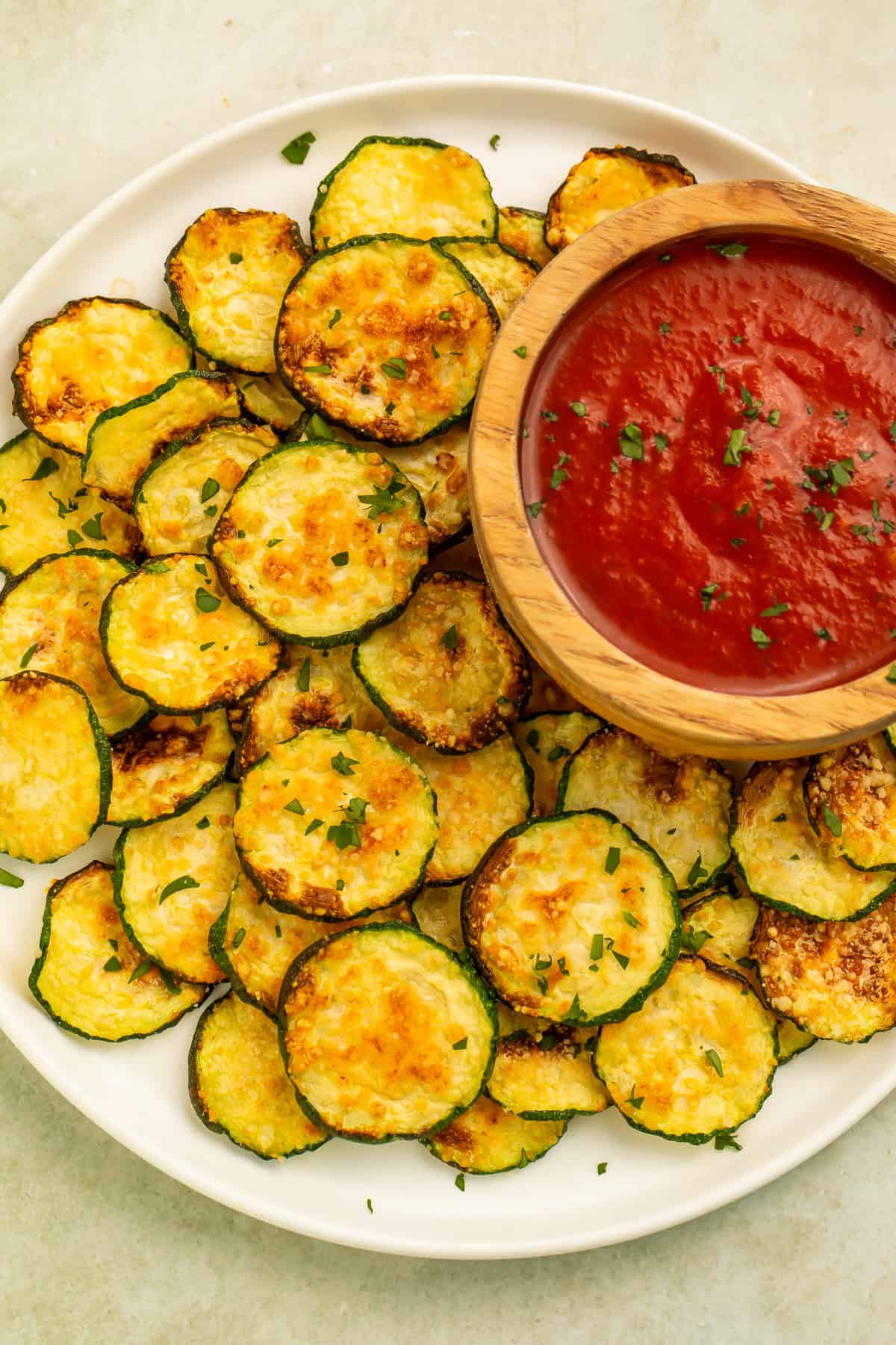 Air fryer zucchini chips served with warm marinara dipping sauce on a white platter.