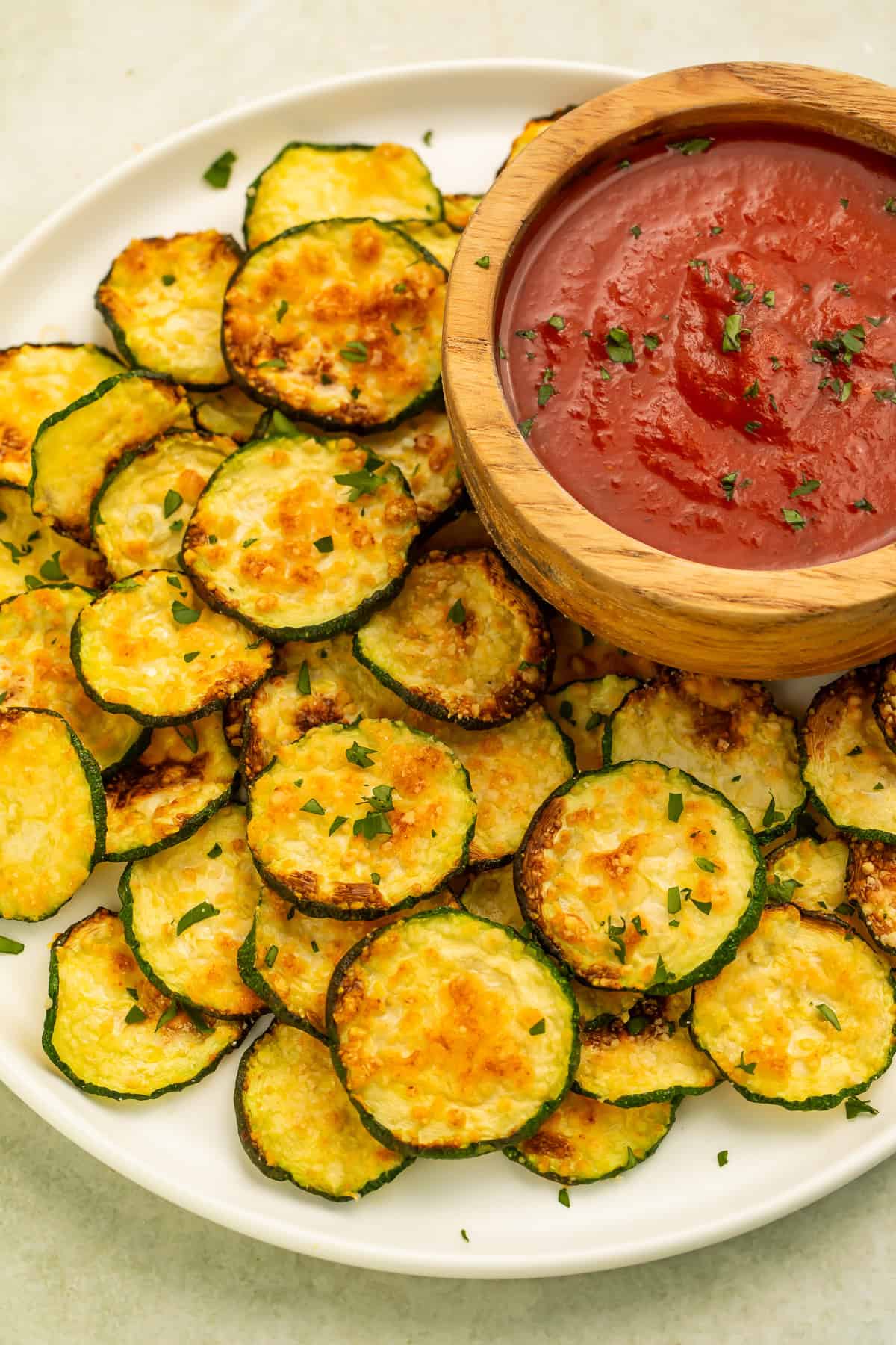 Crispy parmesan air fryer zucchini chips arranged on a platter with marinara sauce.