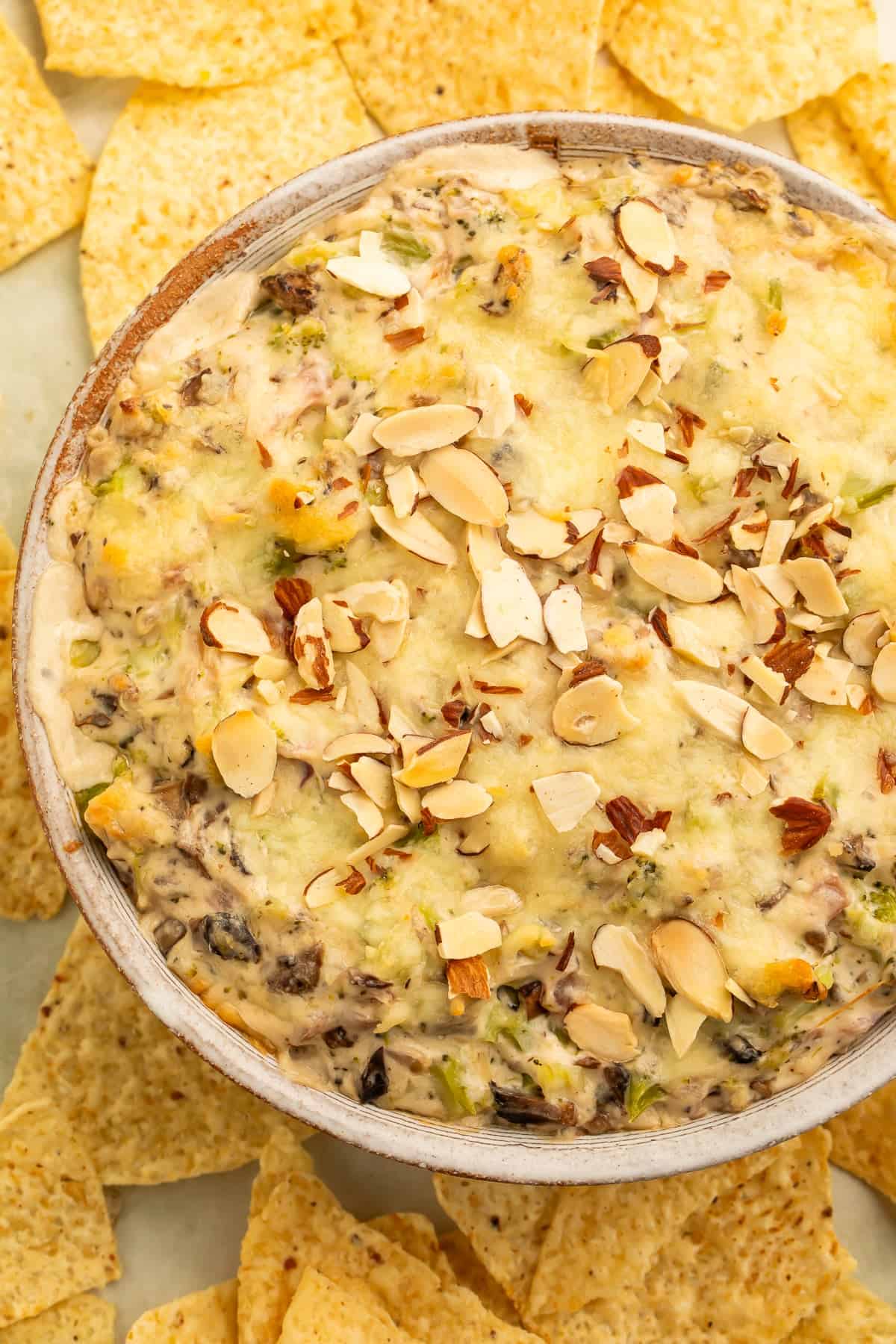 Overhead view of a baked broccoli cheese dip topped with toasted sliced almonds and surrounded by tortilla chips for servin