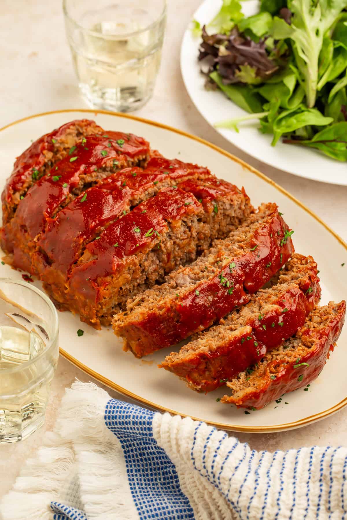 Sliced healthy meatloaf glazed with a glossy tomato sauce and served on a platter with a simple green salad