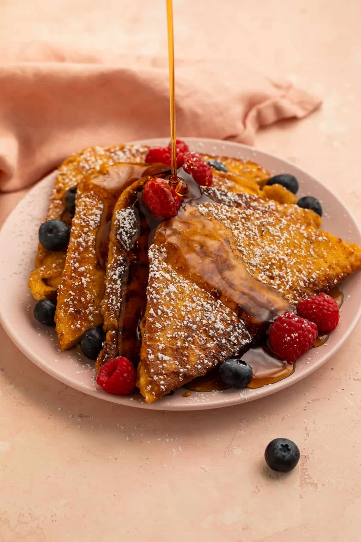 Maple syrup poured over keto French toast topped with fresh raspberries, blueberries, and powdered sweetener.
