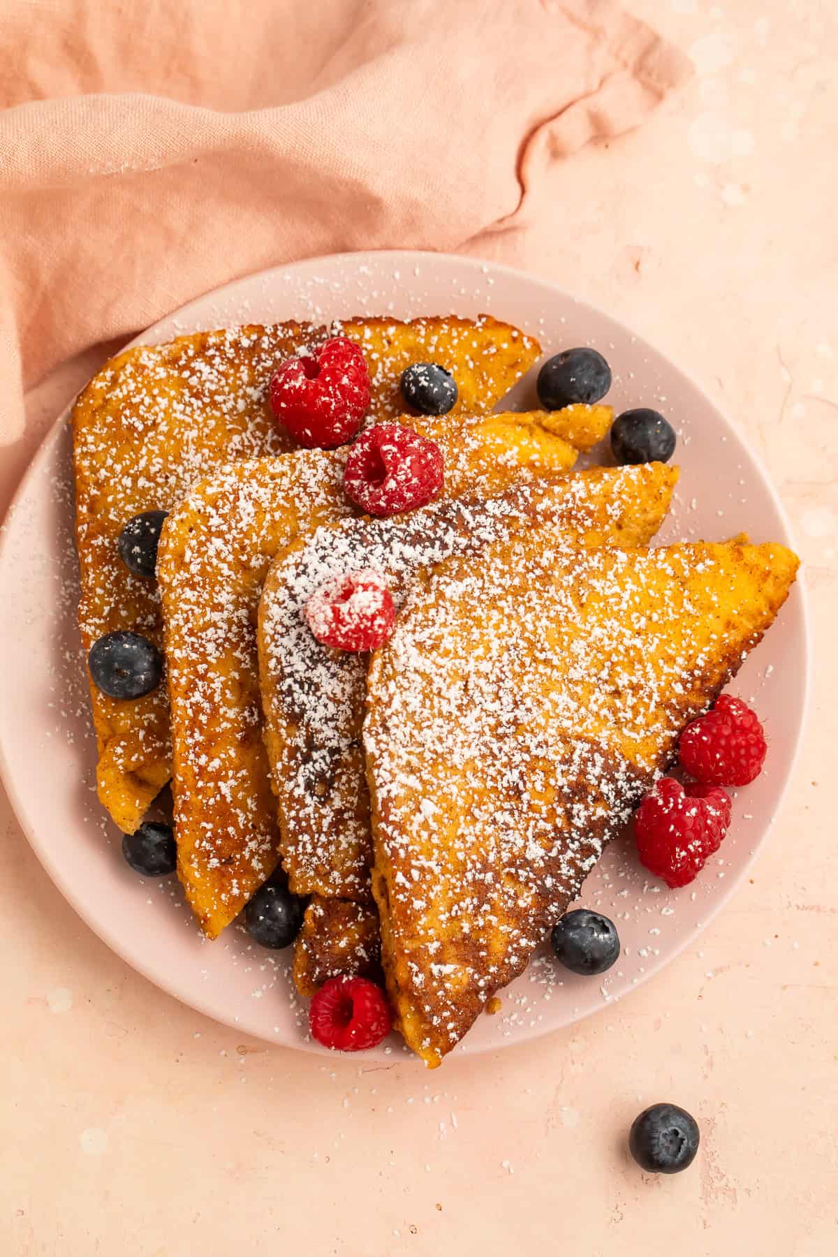 Keto French toast dusted with powdered sweetener and topped with fresh raspberries and blueberries on a pink plate.