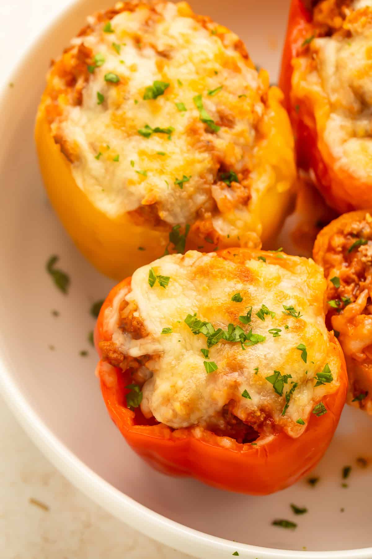 Three baked turkey stuffed bell peppers topped with melted cheese and chopped parsley in a white baking dish.