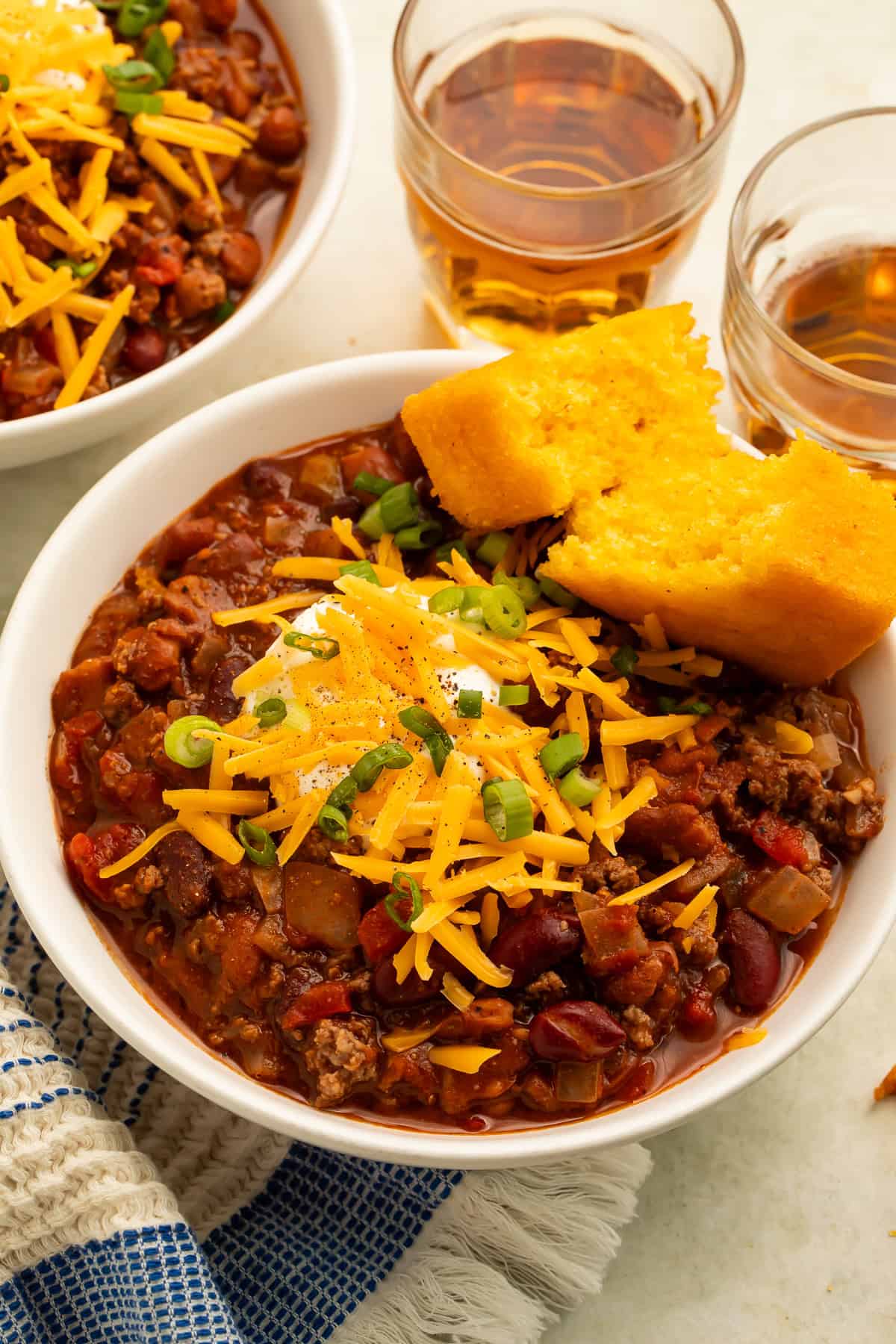 Bowl of ground bison chili topped with cheddar, sour cream, and green onions and served with cornbread.