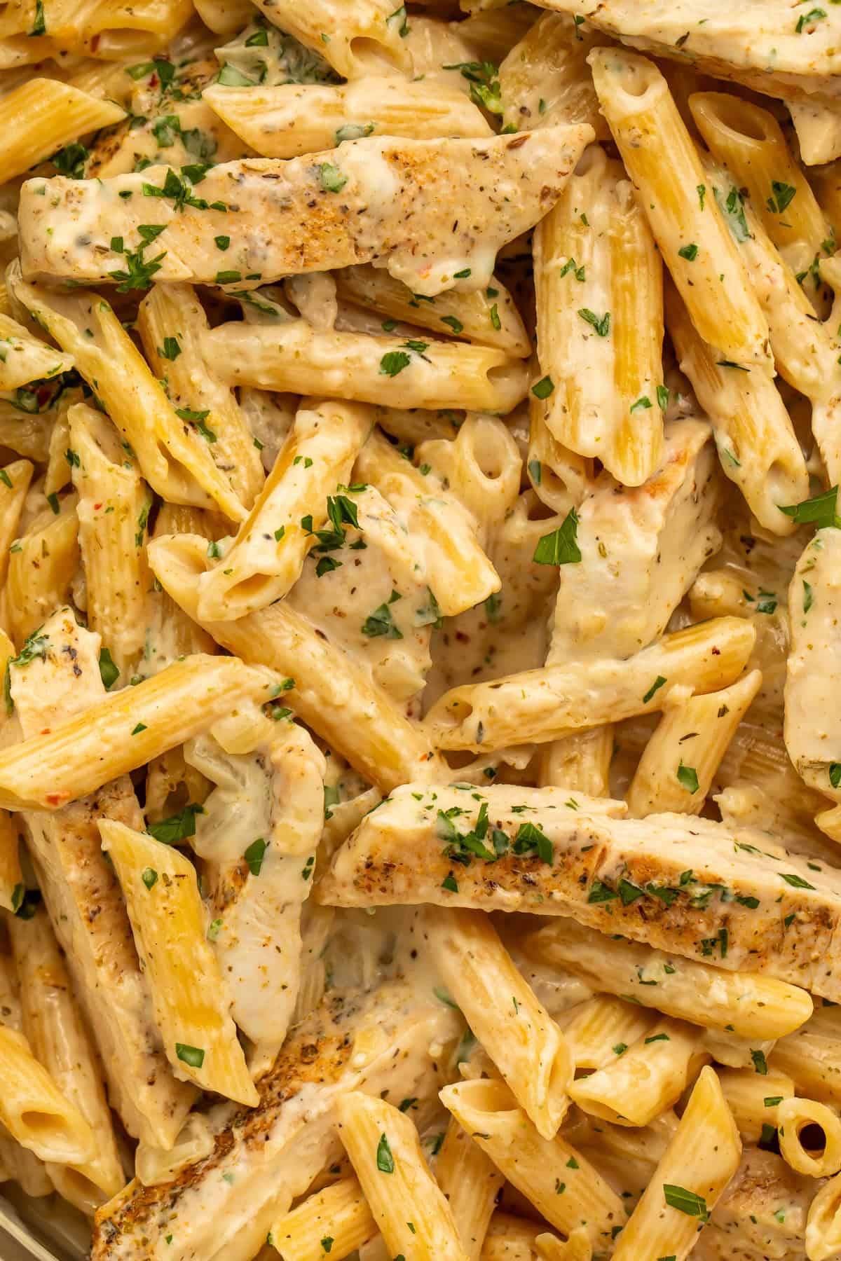 Garlic parmesan chicken pasta with sliced seasoned chicken, penne, creamy sauce, and chopped parsley.