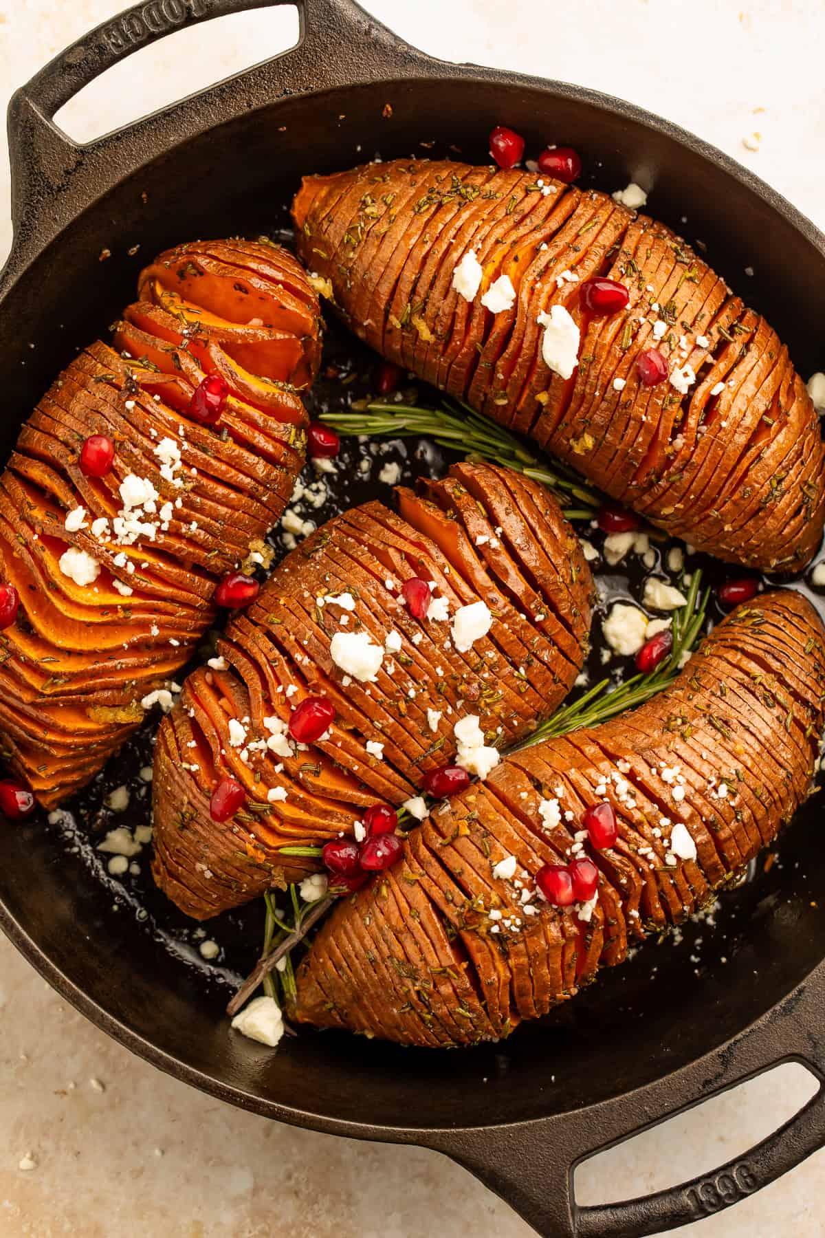 Rosemary maple hasselback sweet potatoes with feta and pomegranate in a cast iron skillet.