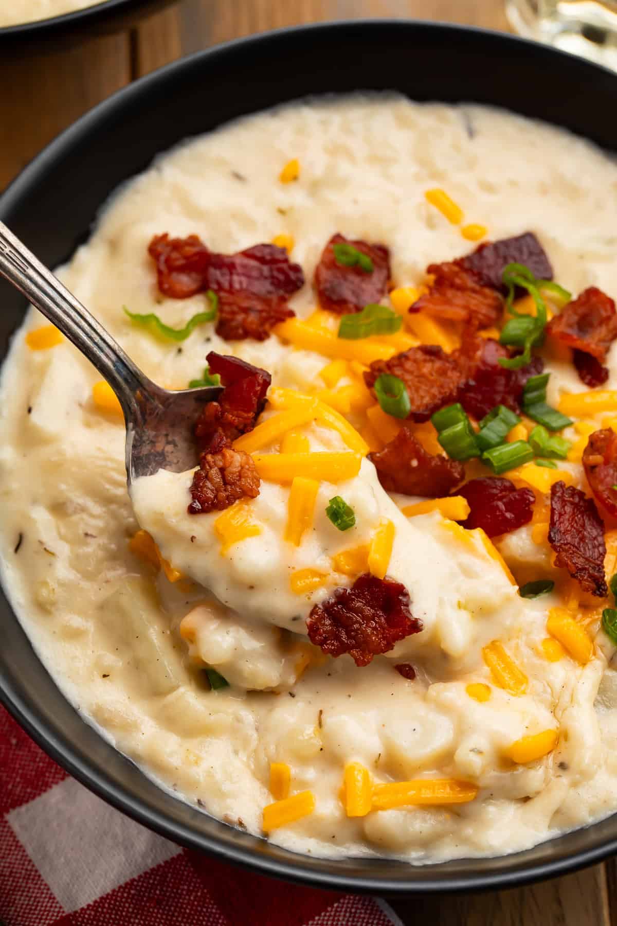 Thick homemade Outback potato soup on a spoon with crispy bacon, shredded cheese, and green onions.