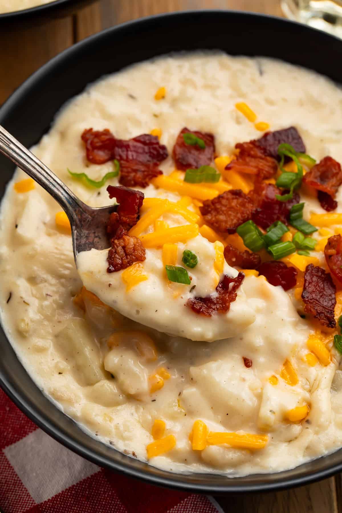 Spoonful of creamy copycat Outback potato soup with potato chunks, bacon, Colby Jack cheese, and green onions.