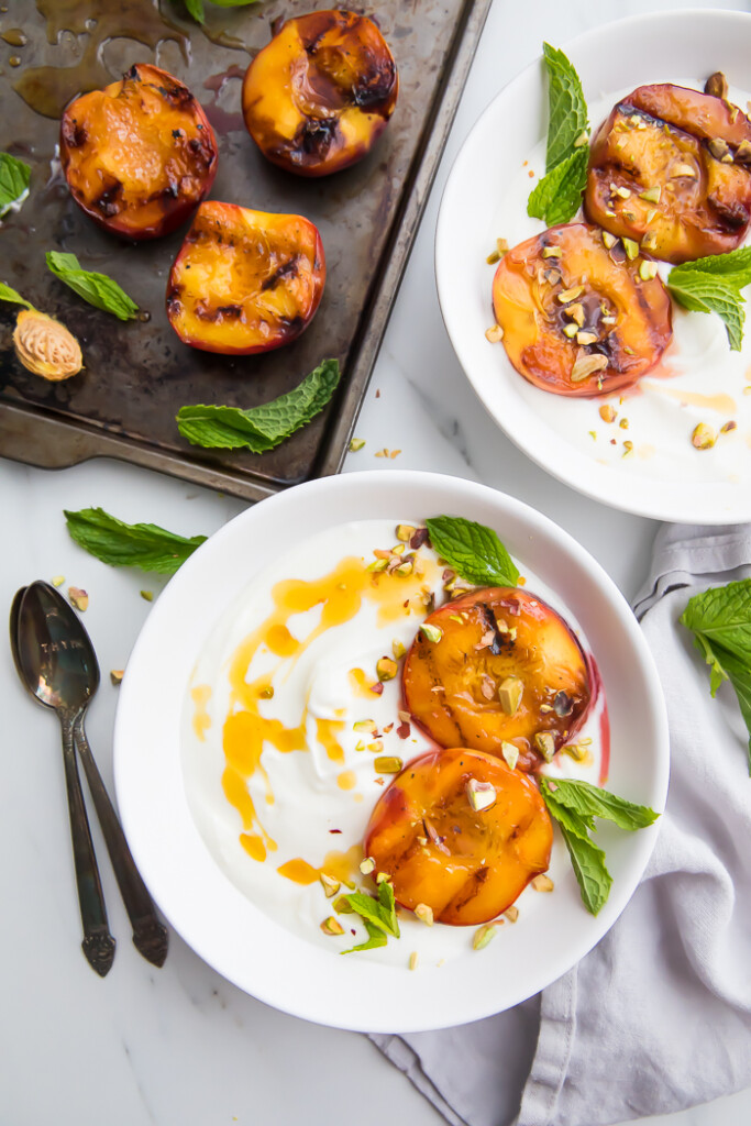 Grilled peaches served on two white plates and drizzled with honey