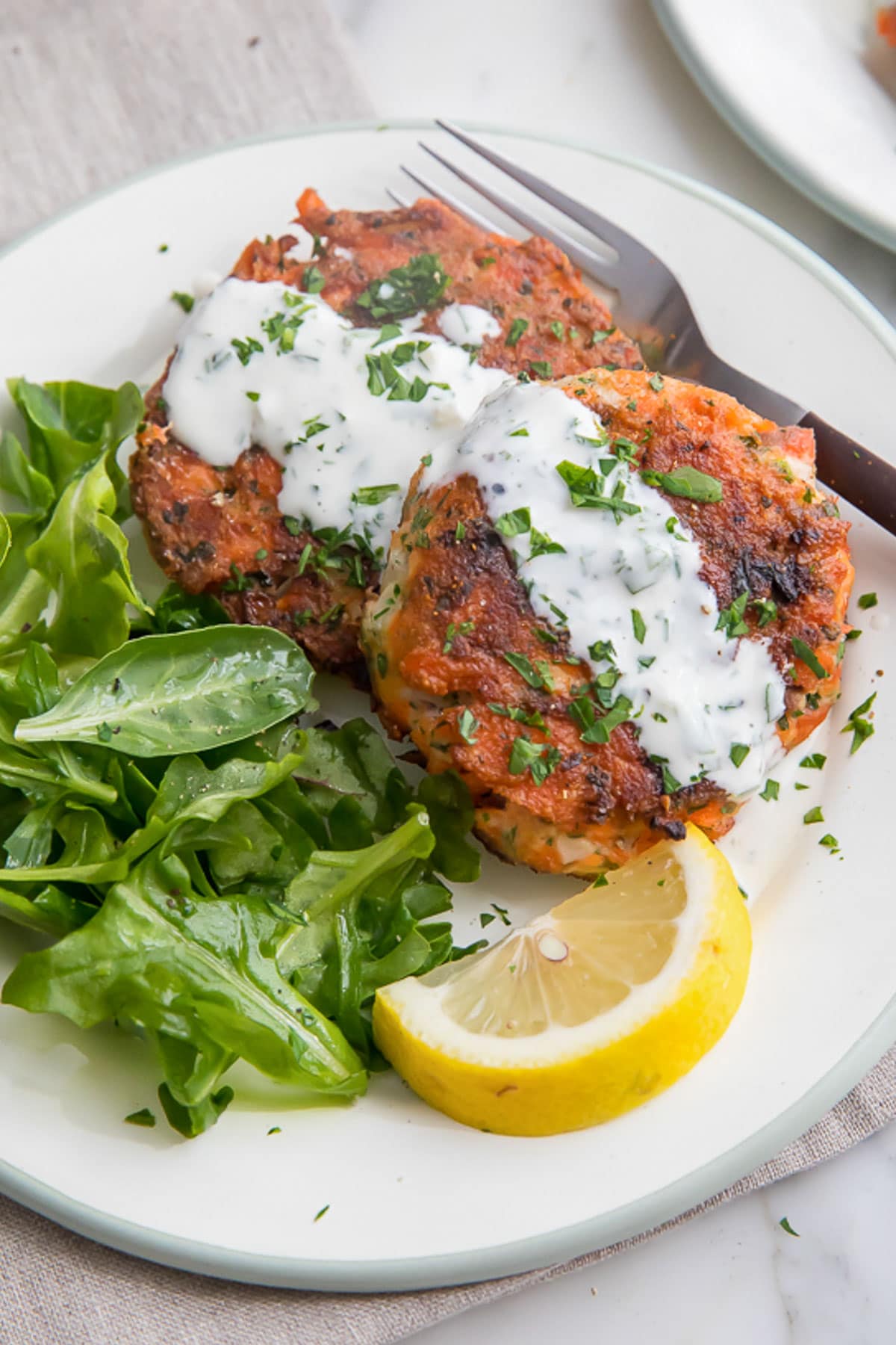 Creamy dill sauce spooned over salmon patties on a white plate.