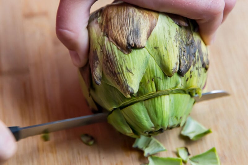 Slice away top two rows of petals from top of artichokes.