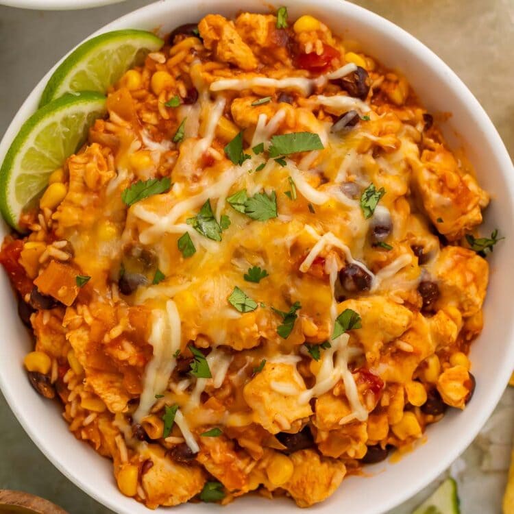 Overhead photo of a chicken burrito bowl with rice, cooked in the Instant Pot, on a table surrounded by lime wedges and a glass of white wine.