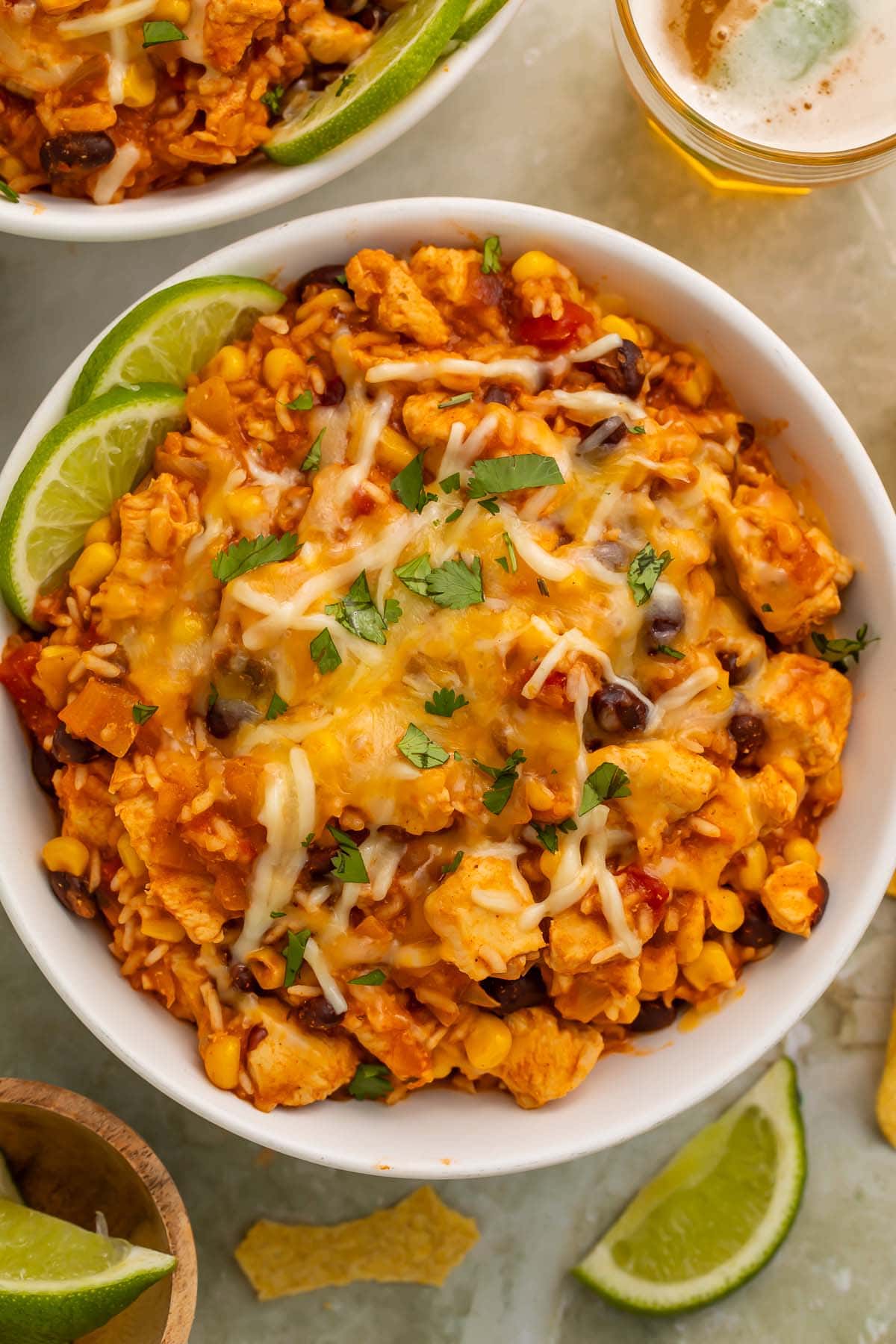 Overhead photo of a chicken burrito bowl with rice, cooked in the Instant Pot, on a table surrounded by lime wedges and a glass of white wine.