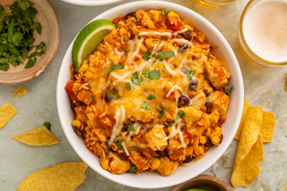 Overhead photo of a chicken burrito bowl with rice, cooked in the Instant Pot, on a table surrounded by lime wedges and a glass of white wine.