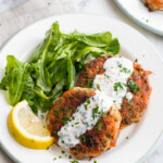 Easy salmon patties on white plate with lemon garlic sauce drizzle and salad.